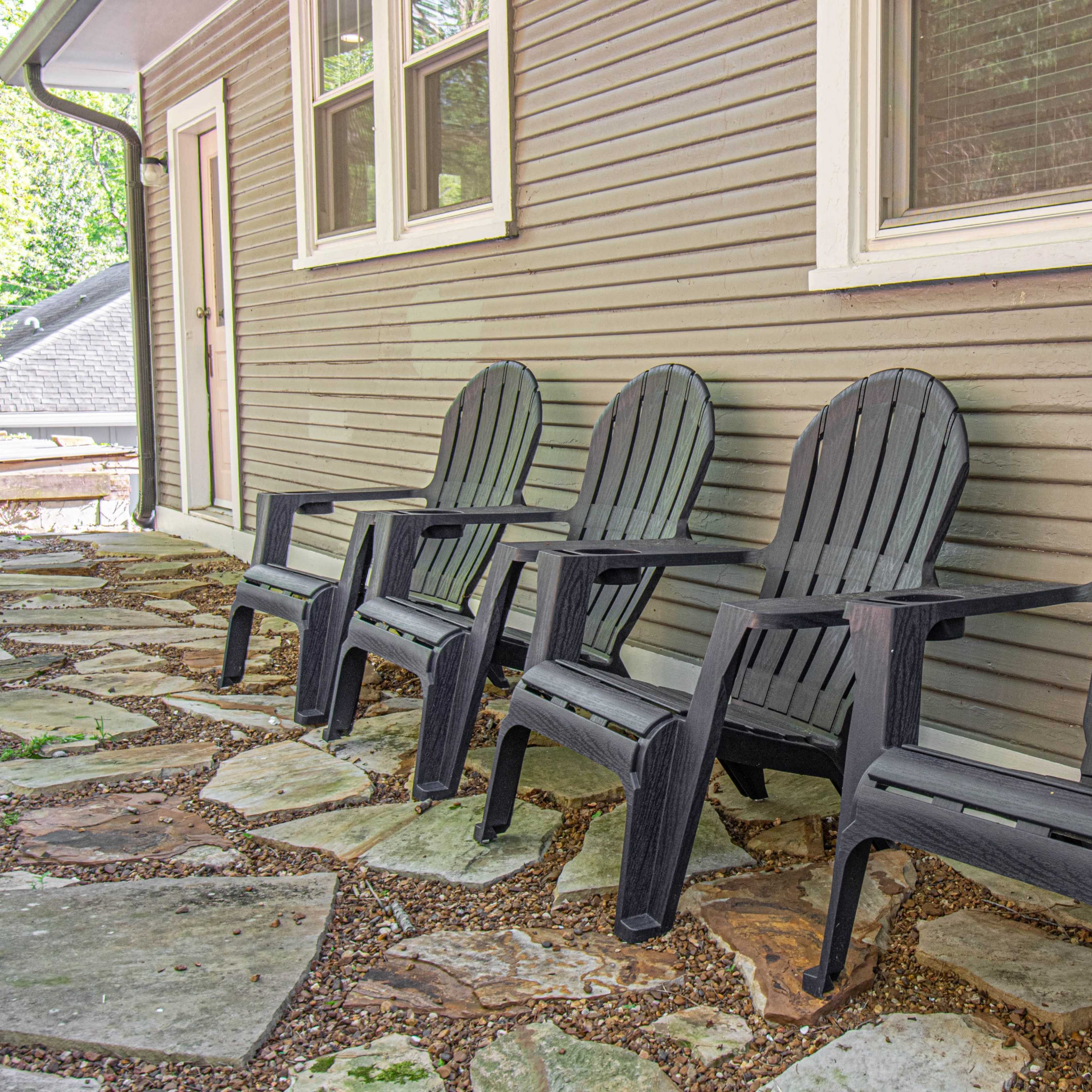 Four black Adirondack chairs are arranged in a line along a stone pathway next to a house.