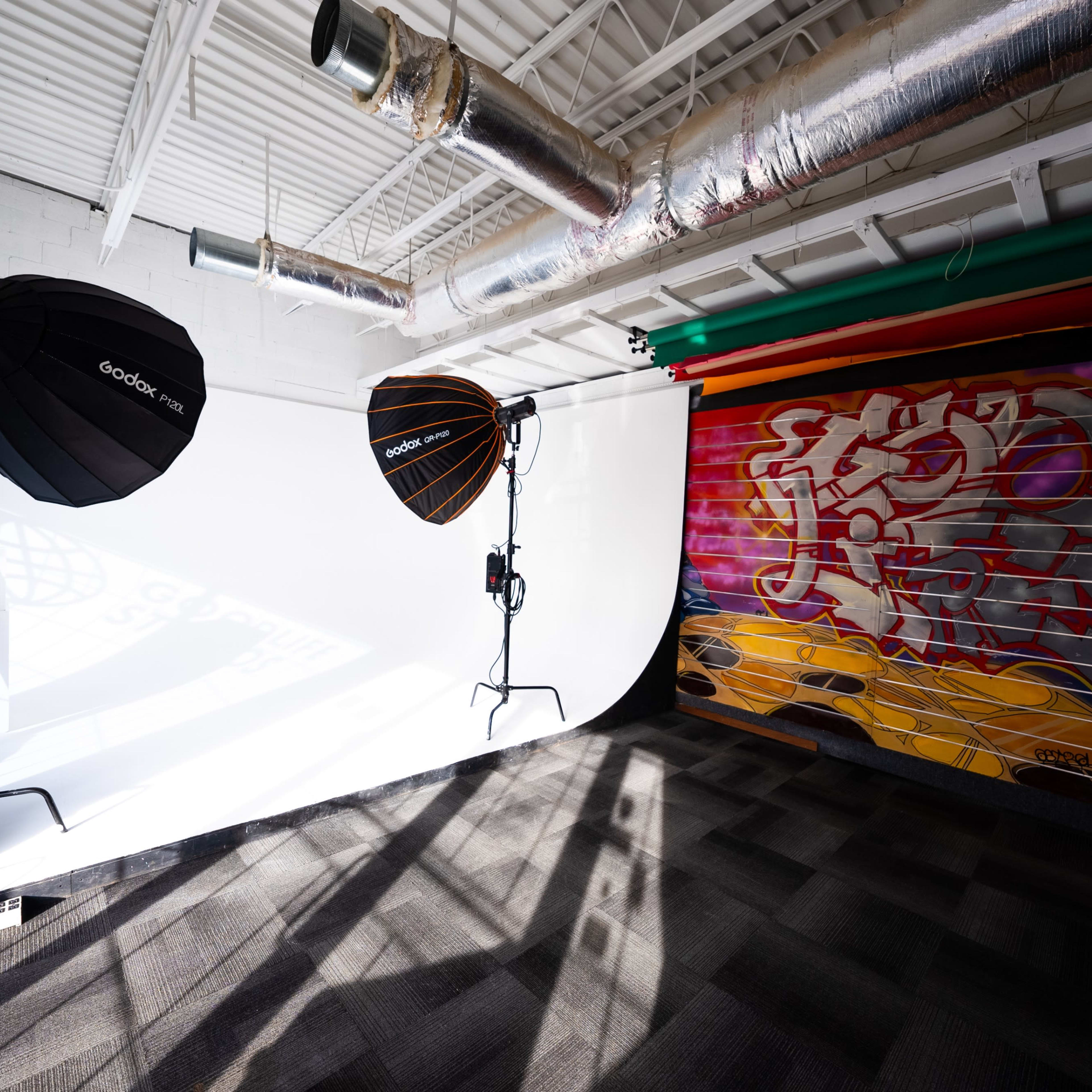 A photography studio with two lighting setups facing a white backdrop, alongside a wall featuring colorful graffiti.