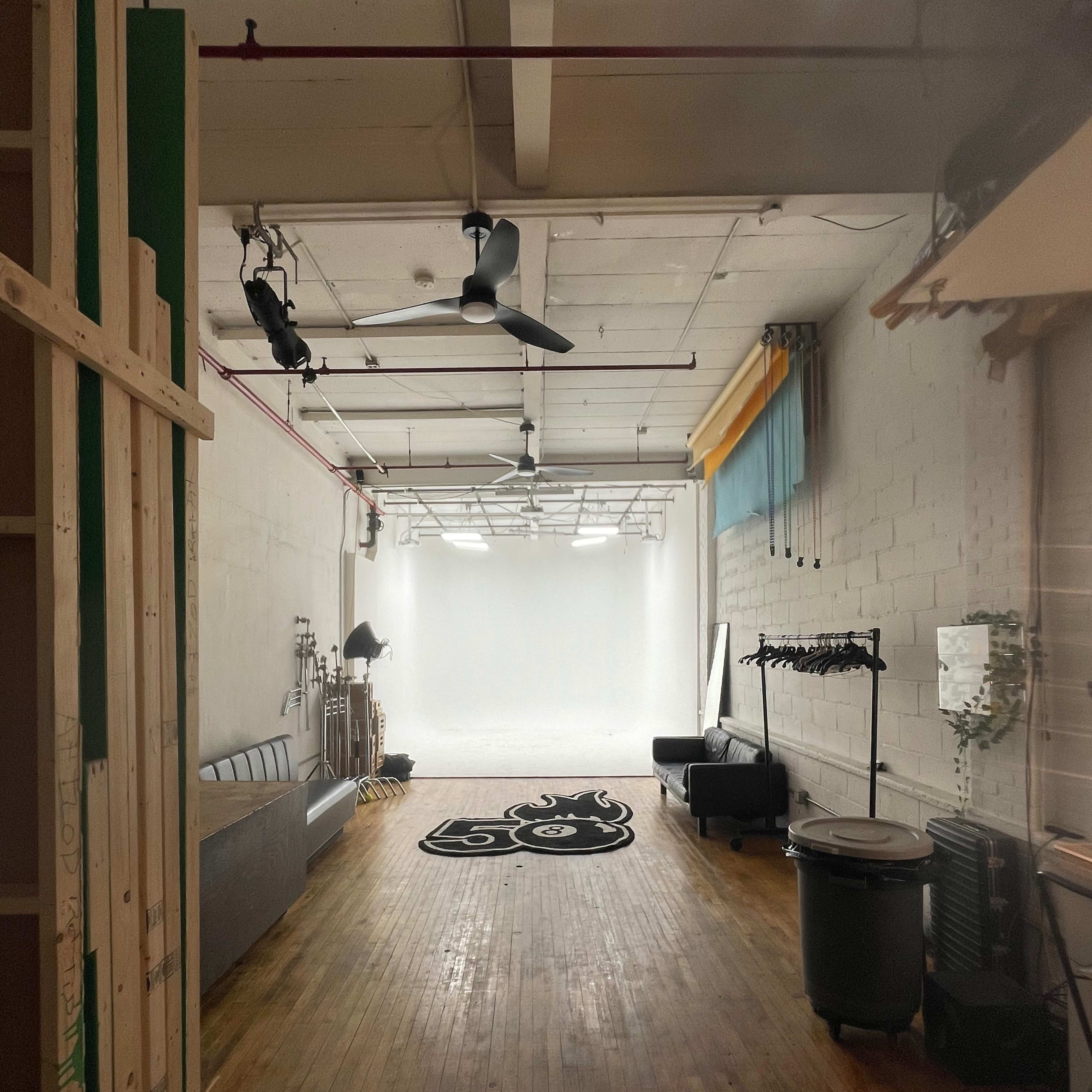 A spacious studio with wooden floors, a gray sofa, and a bright white backdrop at the far end.
