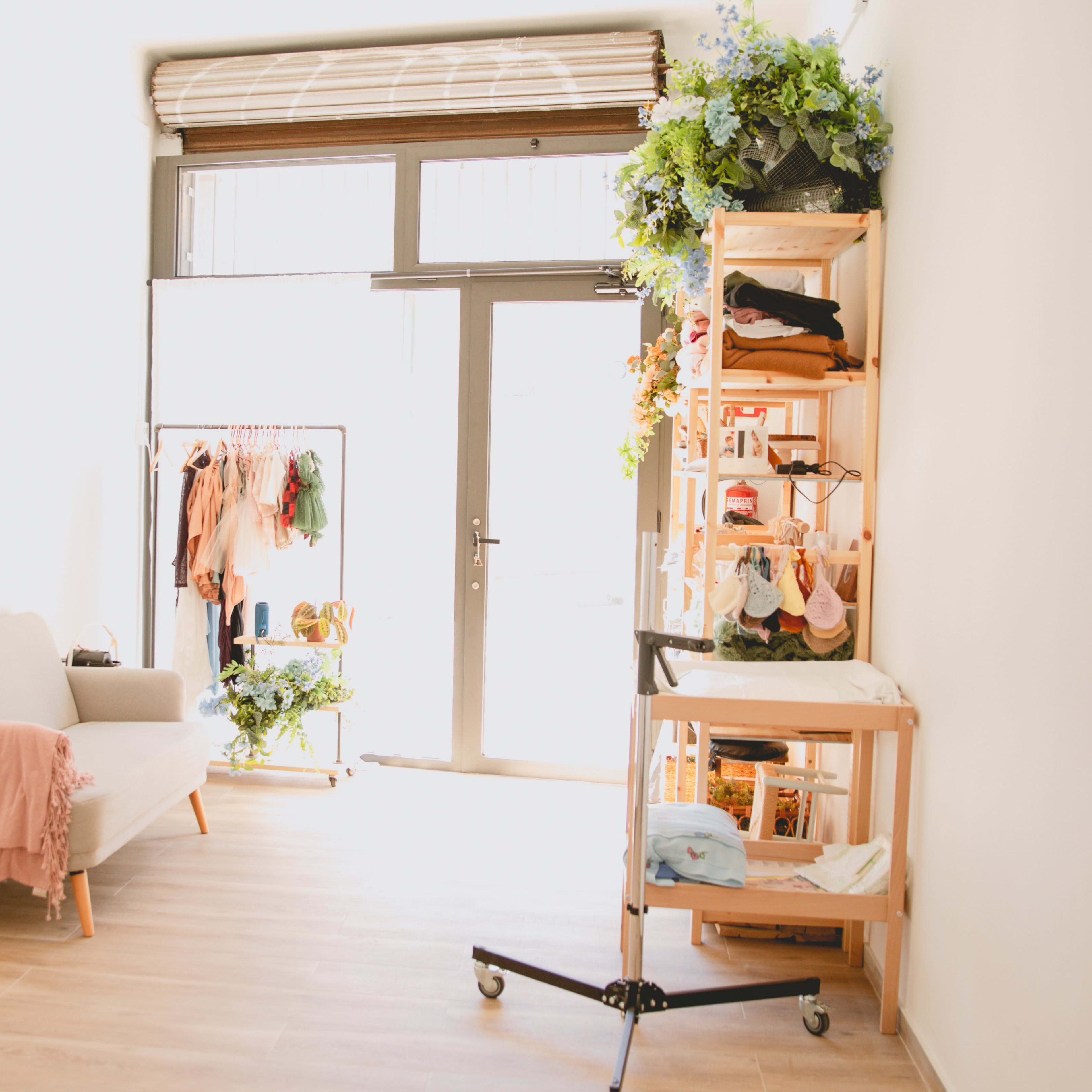 A bright, minimalistic shop interior with a seating area, clothing rack, and a display stand filled with merchandise.