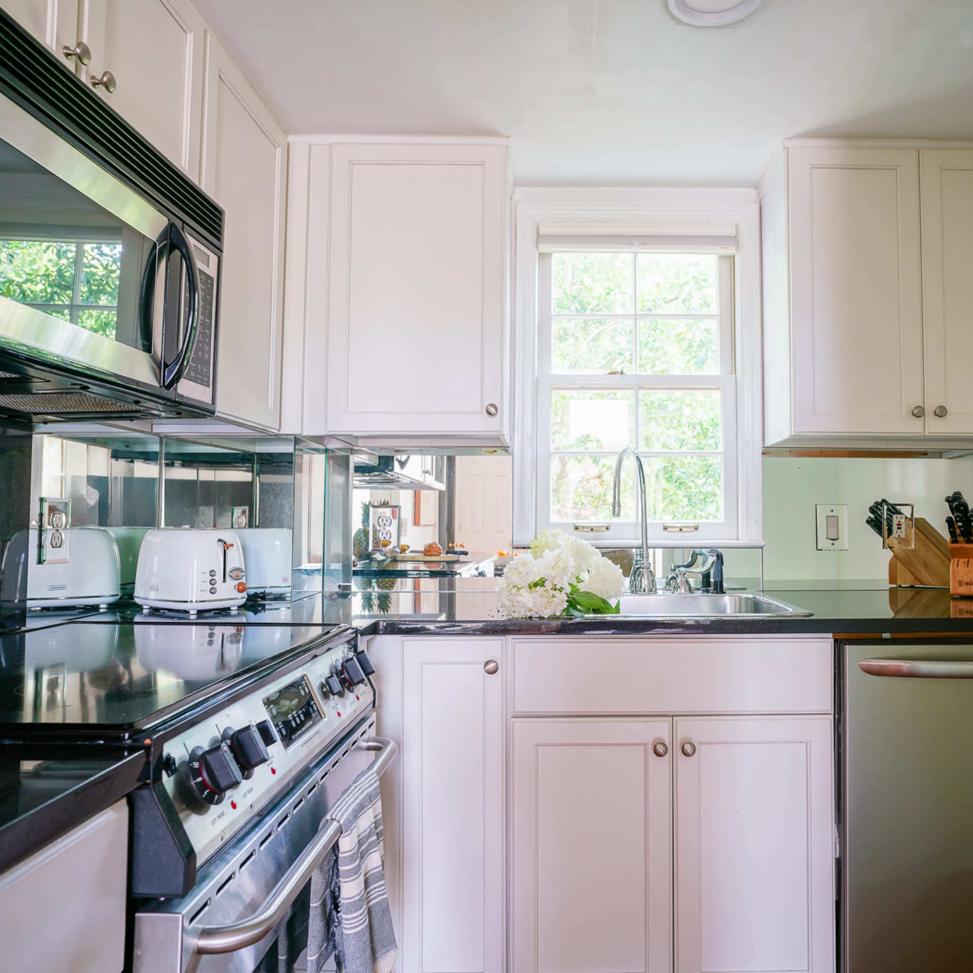 A compact kitchen features black countertops, white cabinetry, and stainless steel appliances, with a window overlooking greenery.