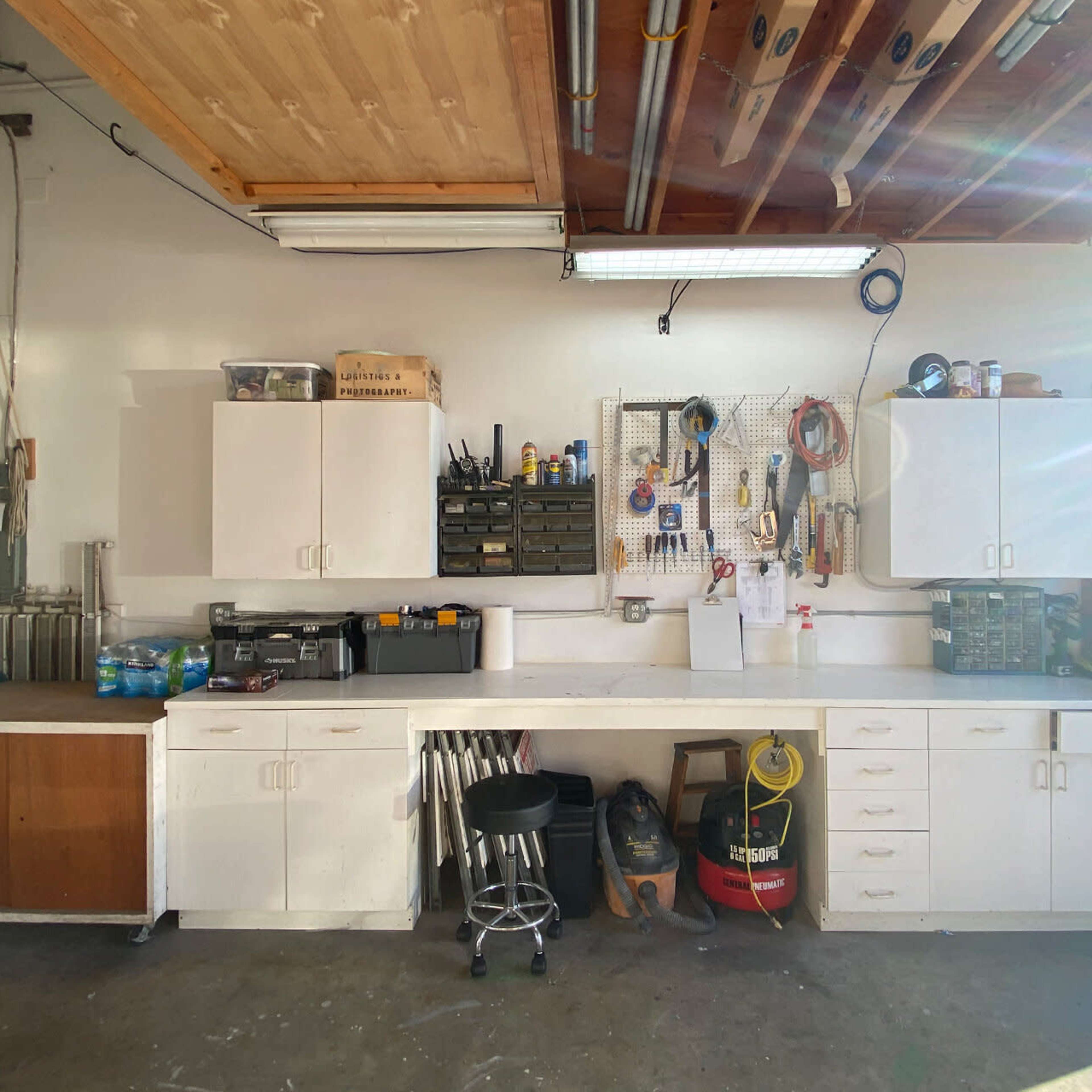 A well-organized workshop with white cabinetry and a counter, filled with tools and equipment.