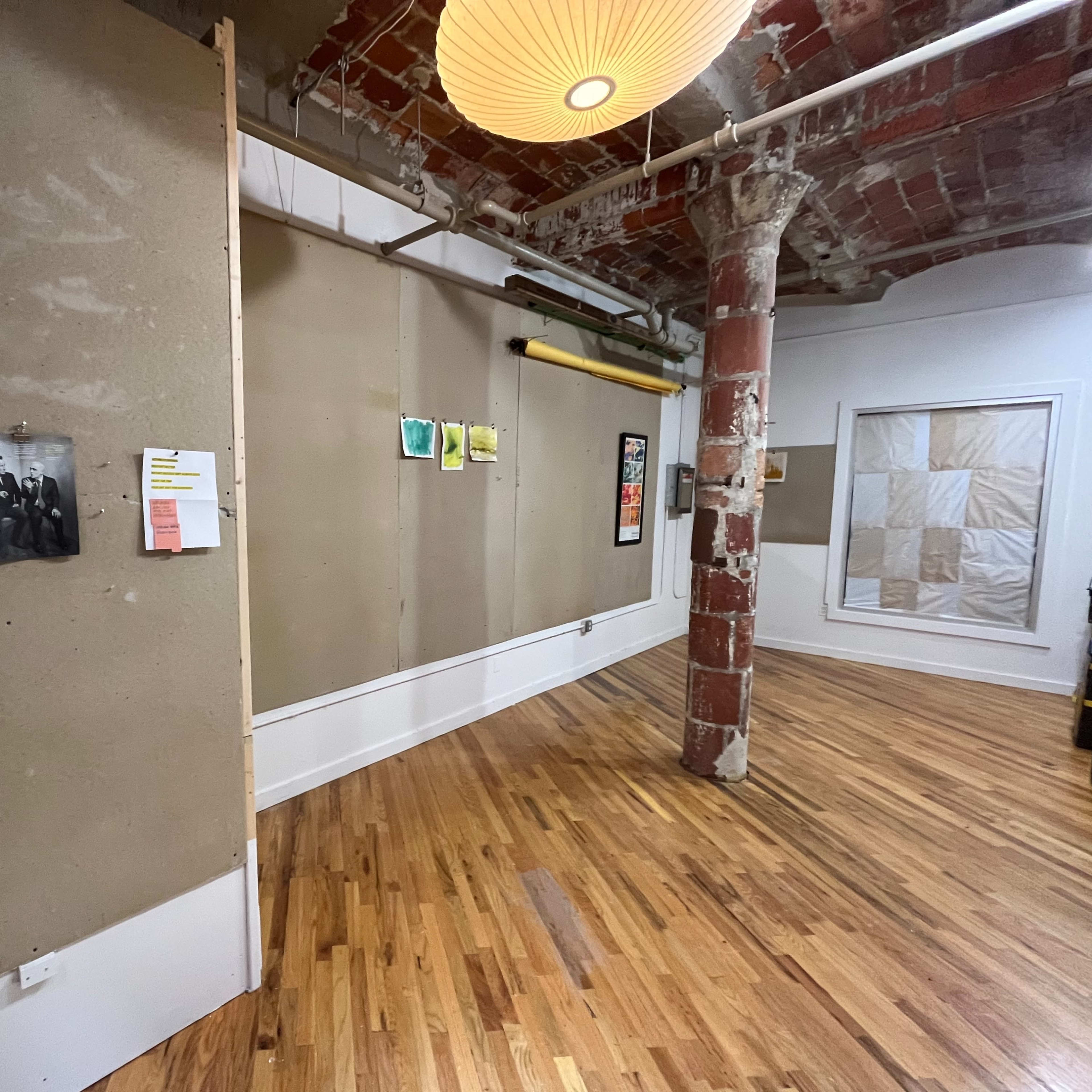 A minimalist interior space with bare walls, wooden flooring, and a mix of artwork and photographs displayed.