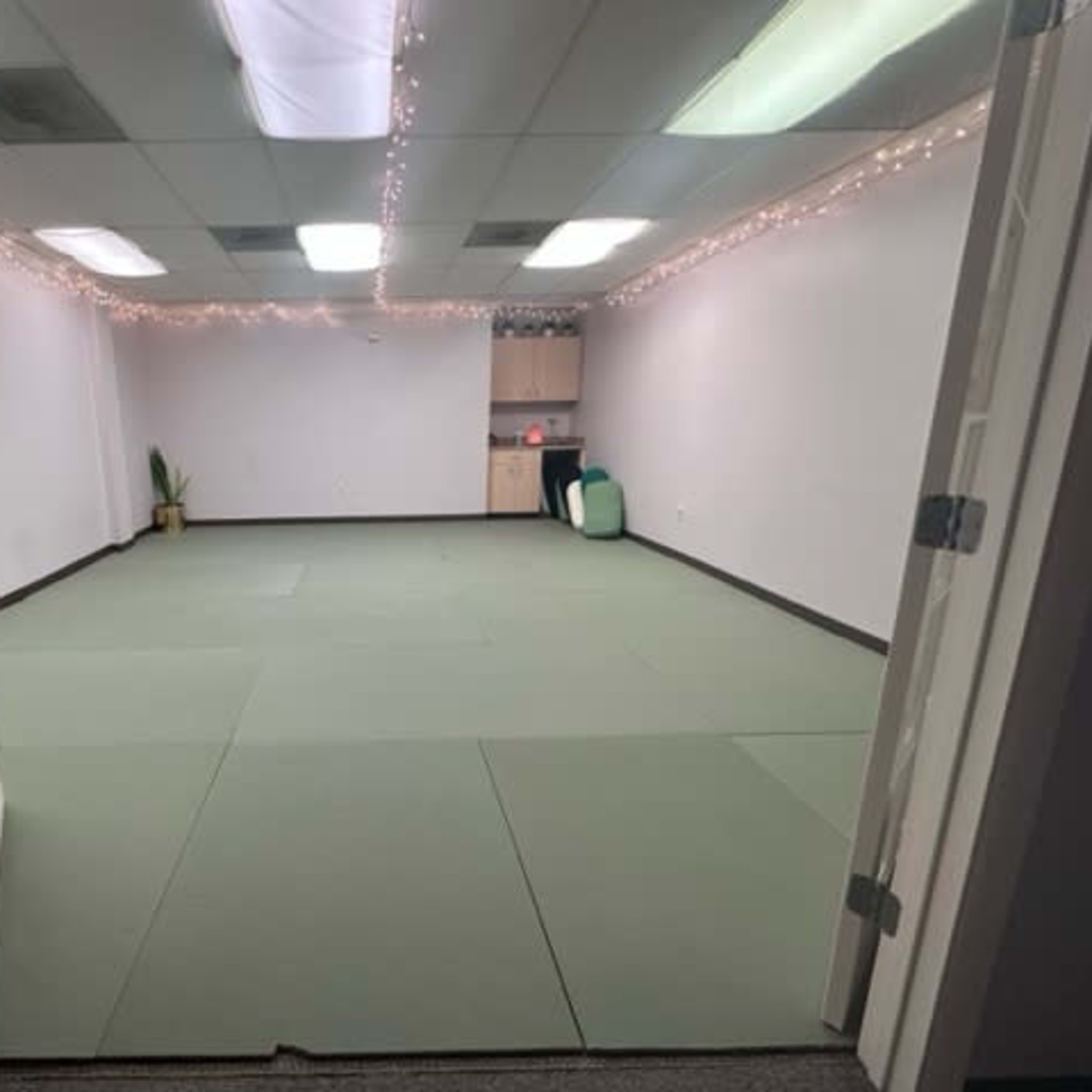 An empty room with green mats on the floor, white walls, and decorative string lights along the ceiling.