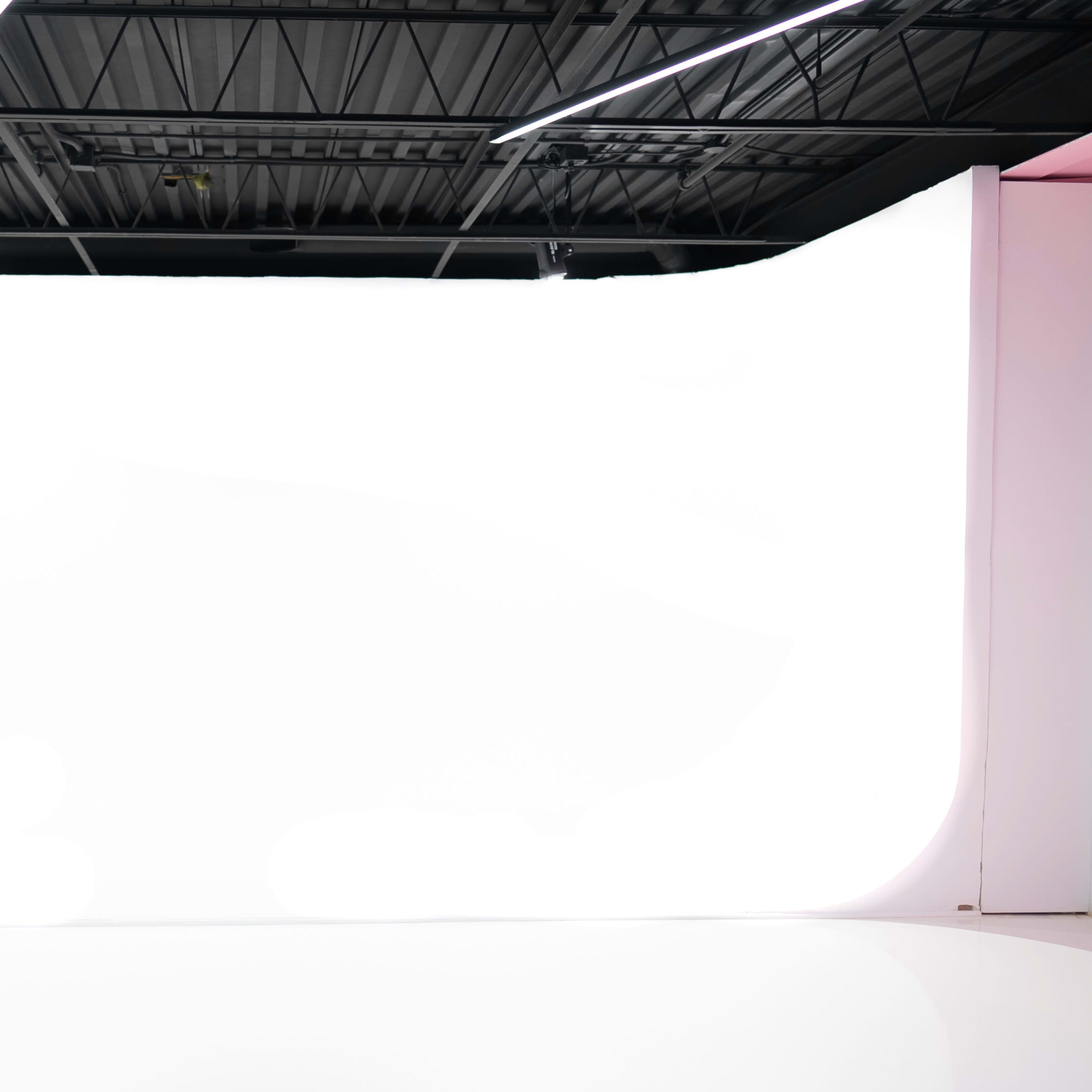 A spacious, empty studio with a large white backdrop and modern lighting fixtures.