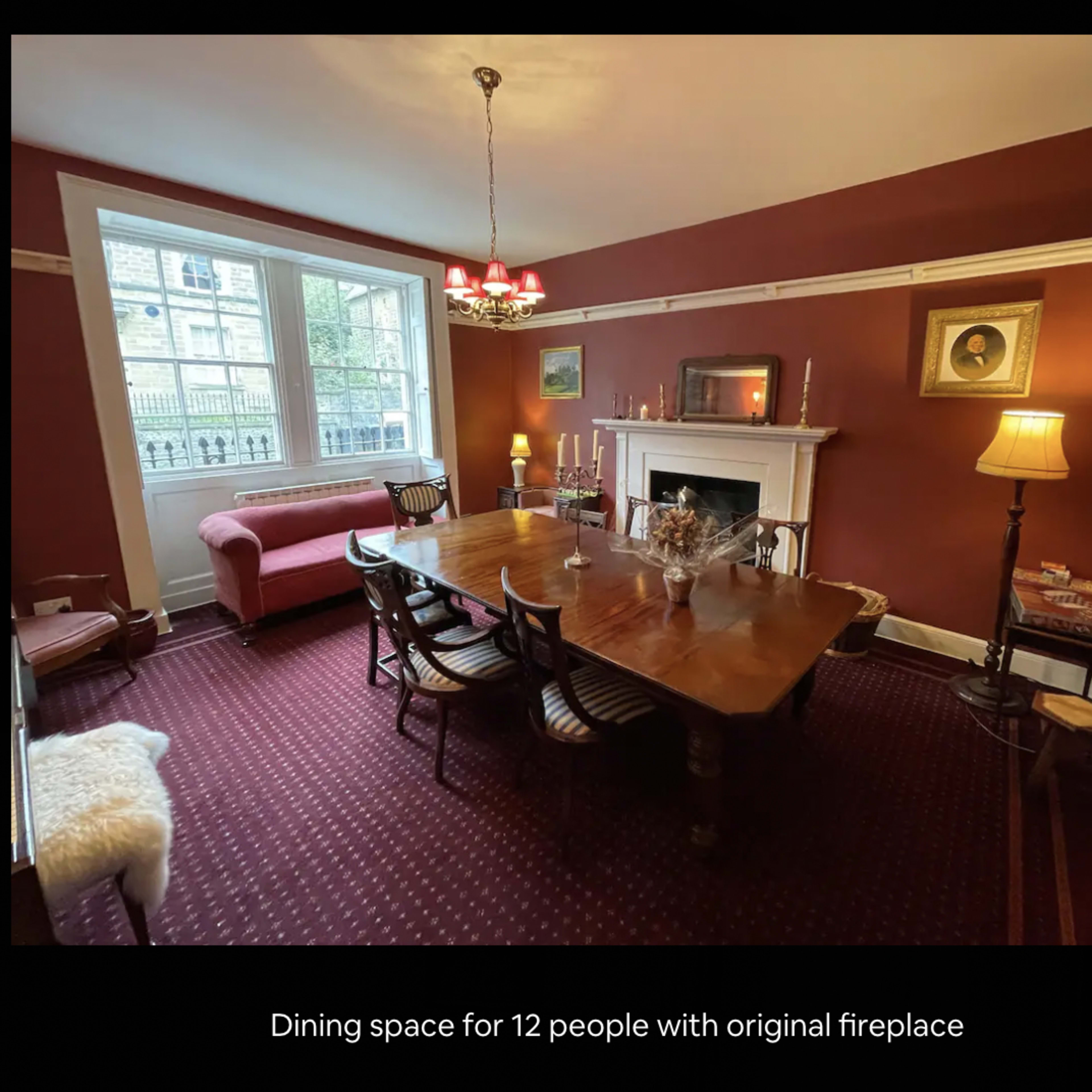 A dining room featuring a wooden table set for twelve, an original fireplace, and a mix of lighting fixtures.