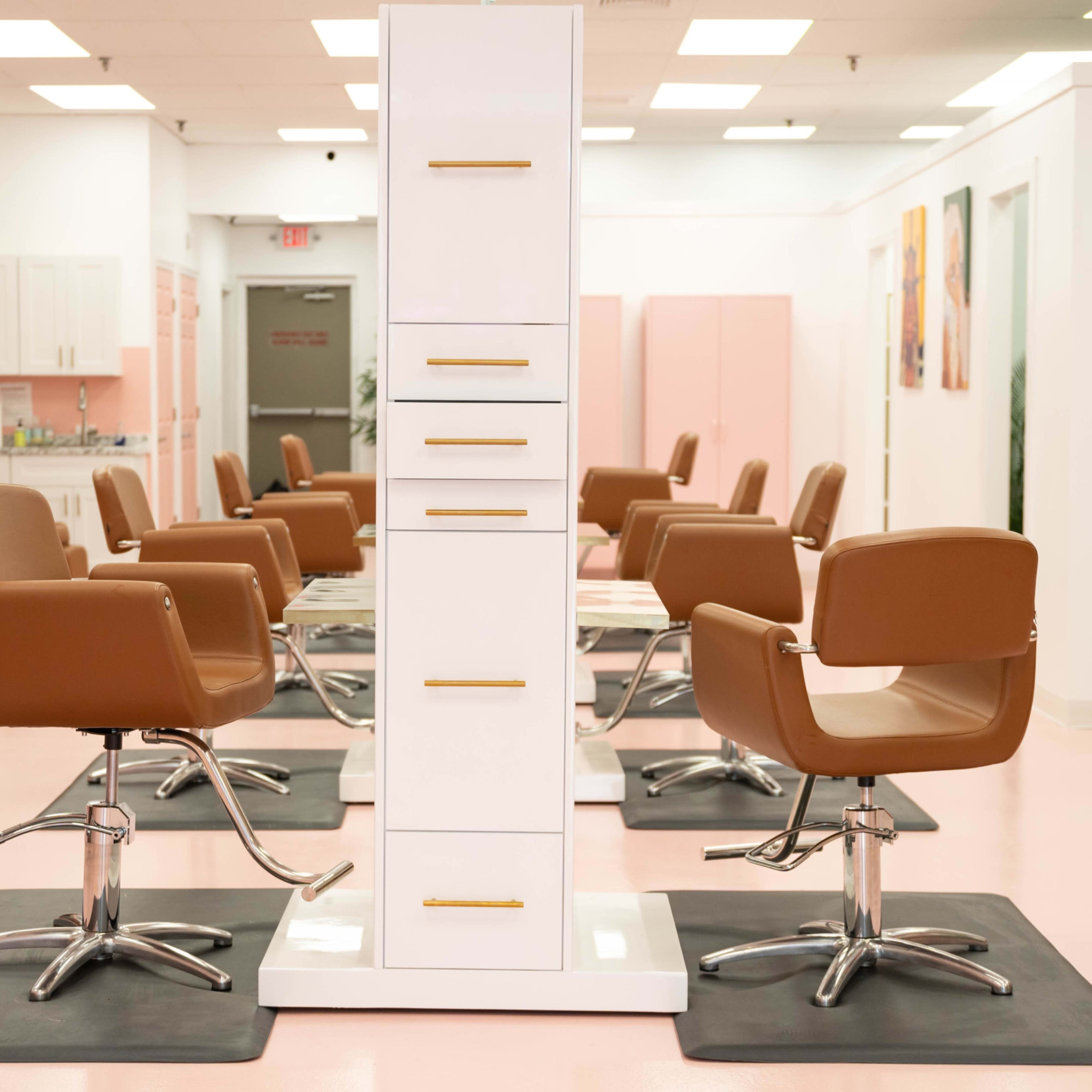 A modern hair salon with several styling chairs arranged around a central storage unit.