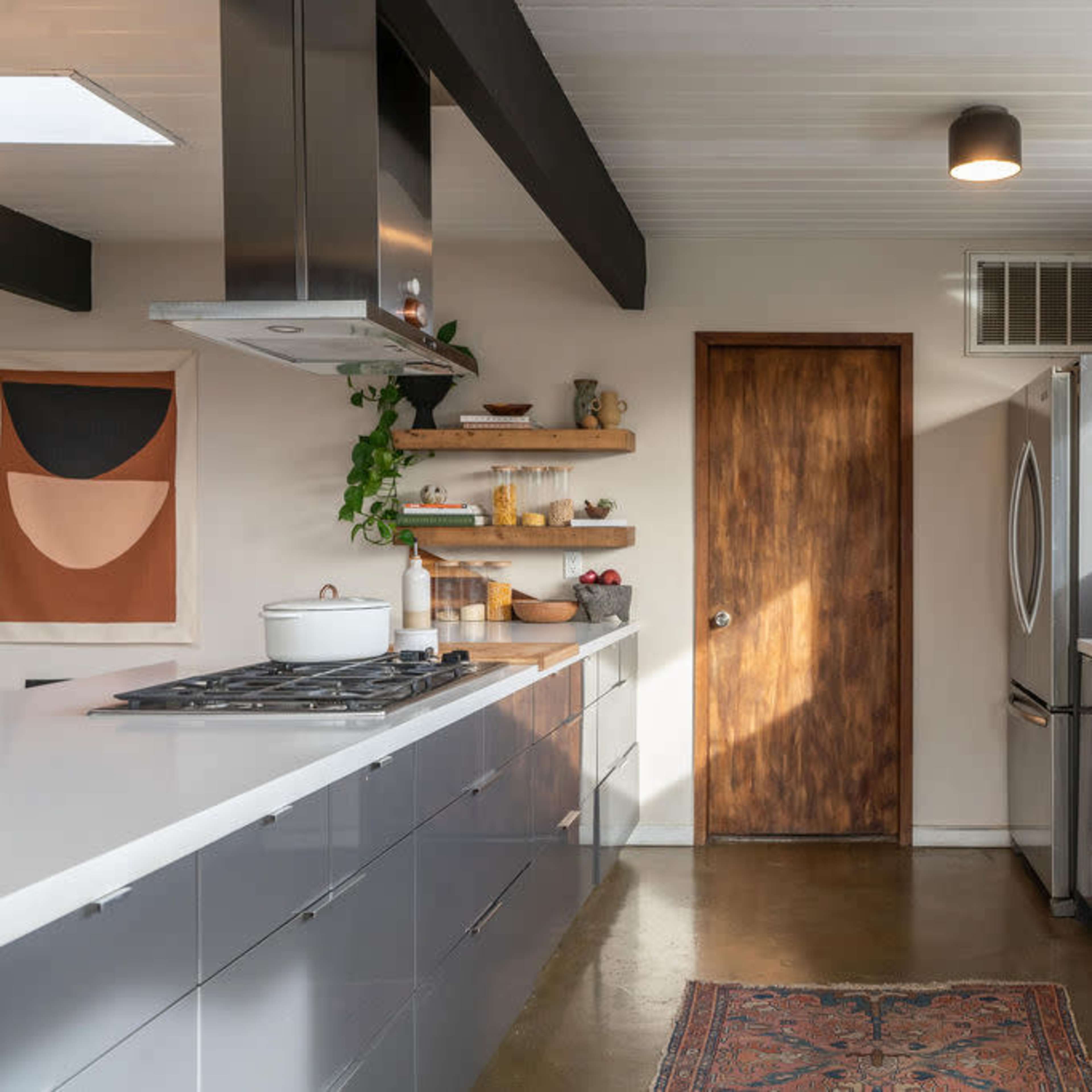 A modern kitchen featuring gray cabinetry, a stainless steel refrigerator, a gas stove, and a wooden door leading to another area.