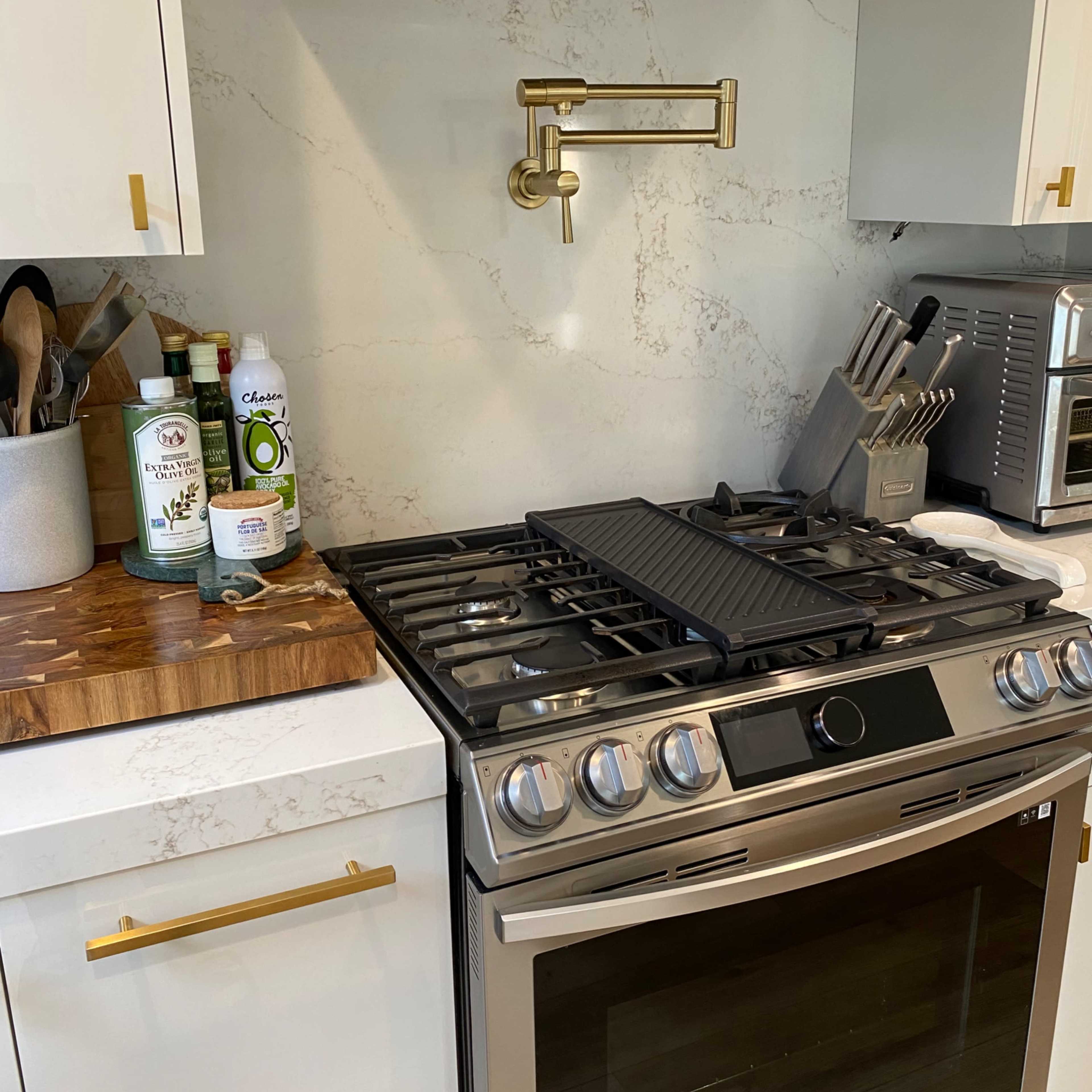 A modern kitchen with a stainless steel gas stove, a marble backsplash, and a wooden cutting board on the counter.