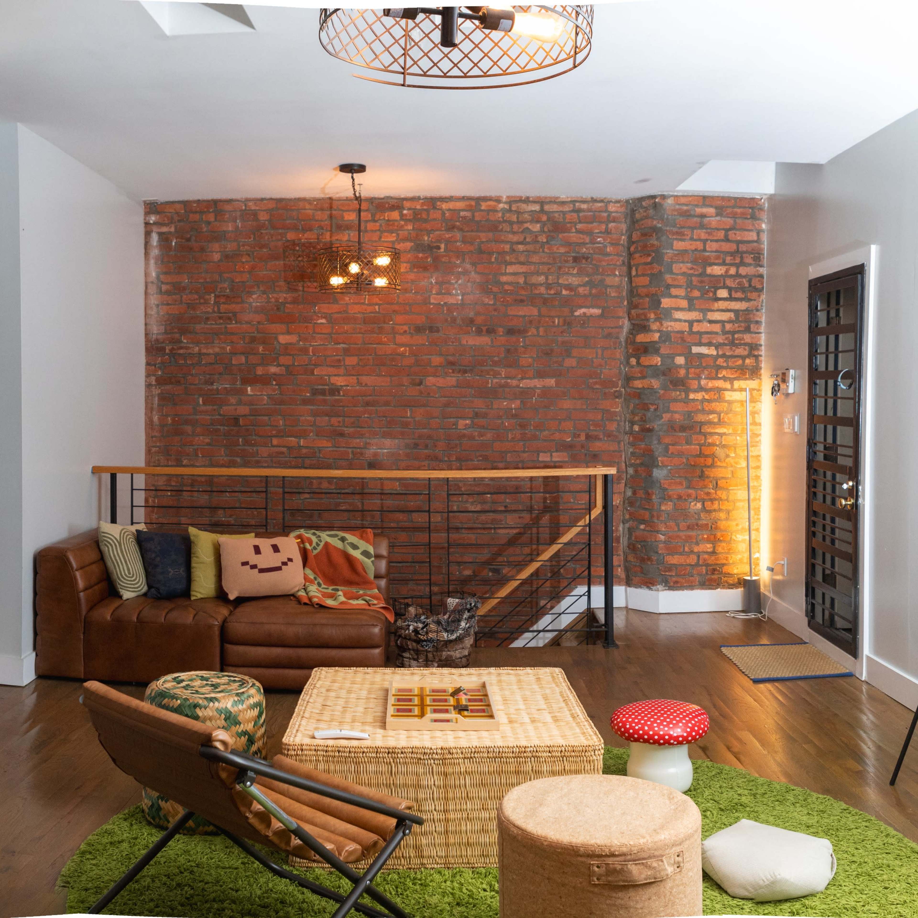 A modern living room with a brown leather sofa, a round green rug, and a large brick wall, complemented by a unique wall art piece and a contemporary light fixture.