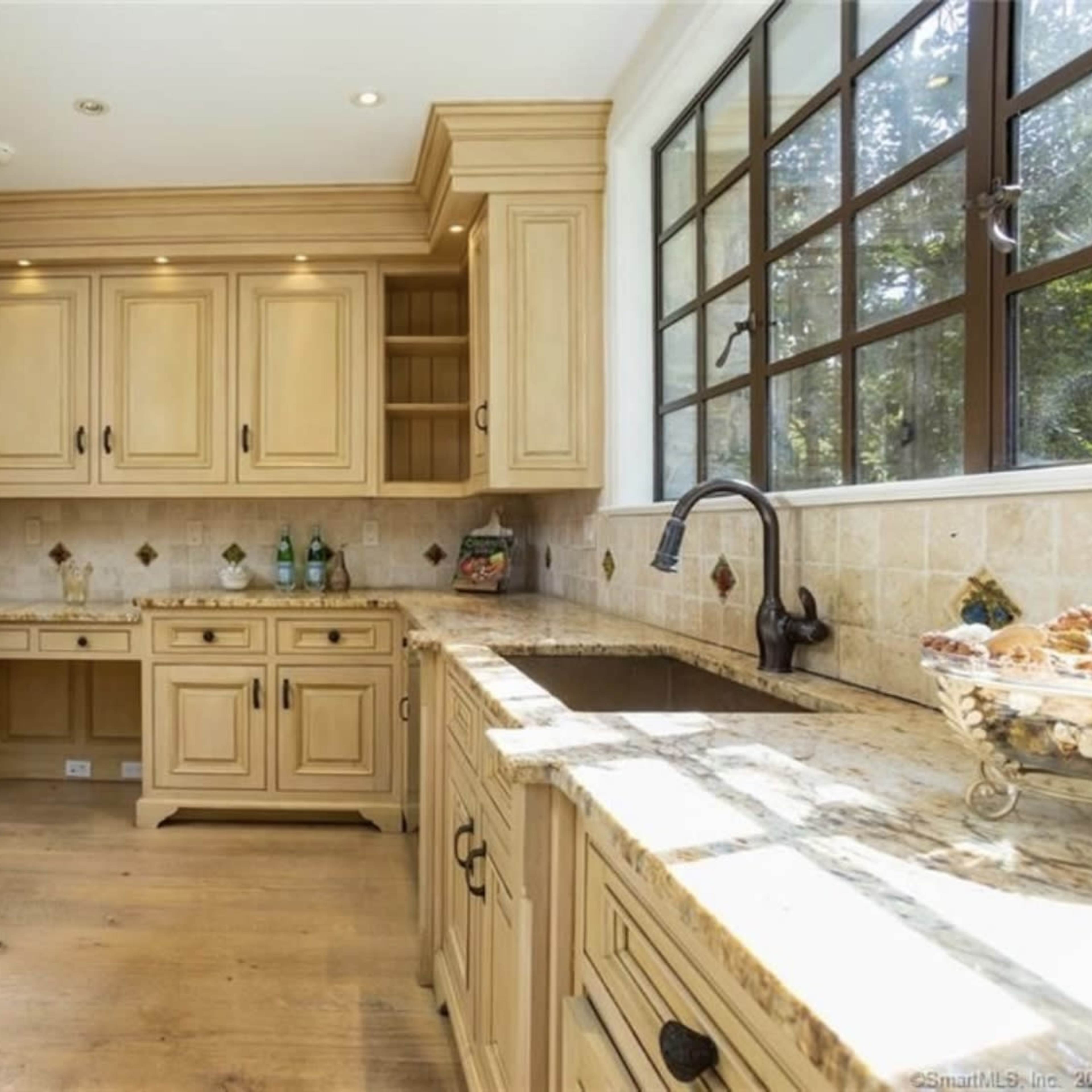 A kitchen with light-colored wooden cabinetry, granite countertops, and a large window providing natural light.