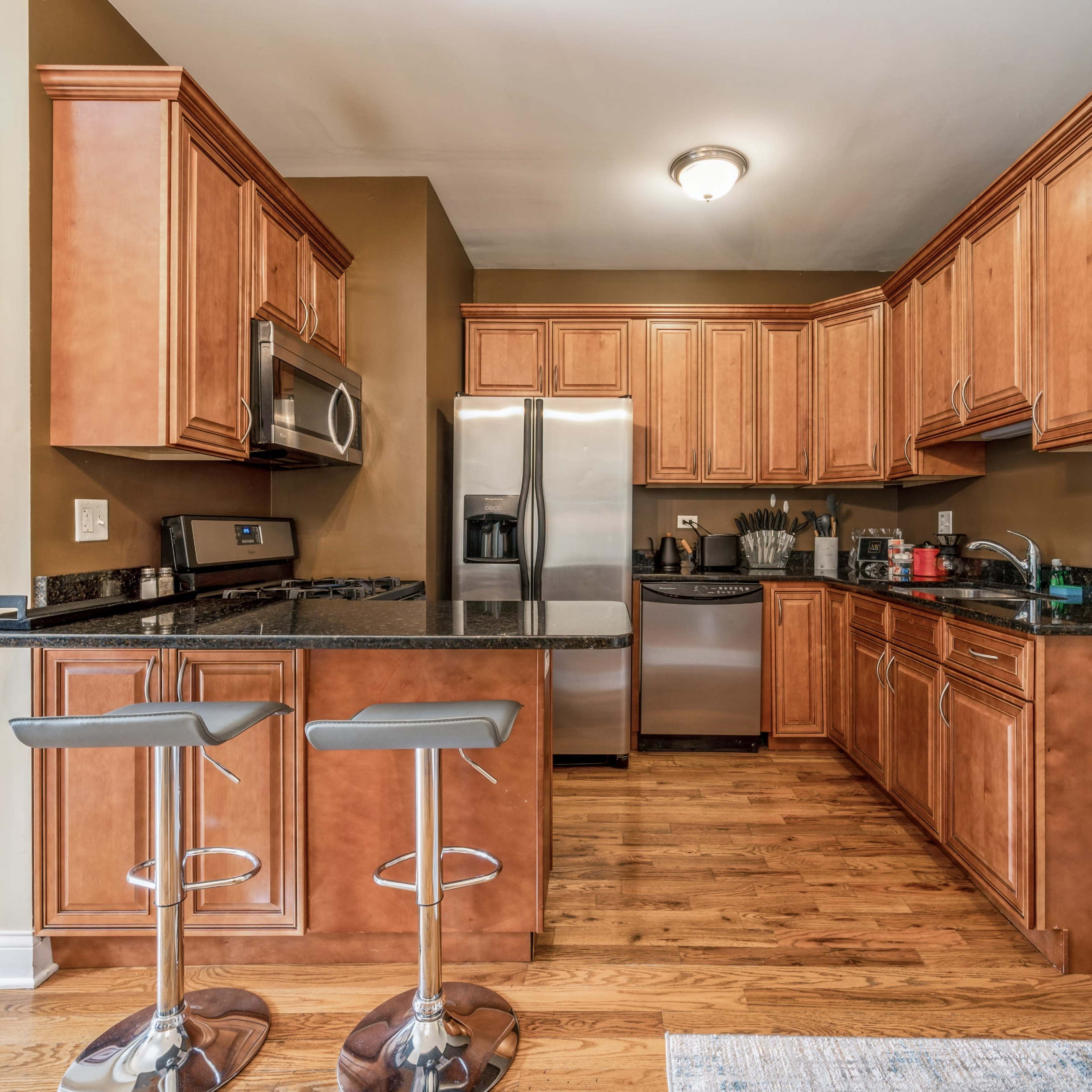 A kitchen featuring wooden cabinets, black granite countertops, stainless steel appliances, and barstool seating.