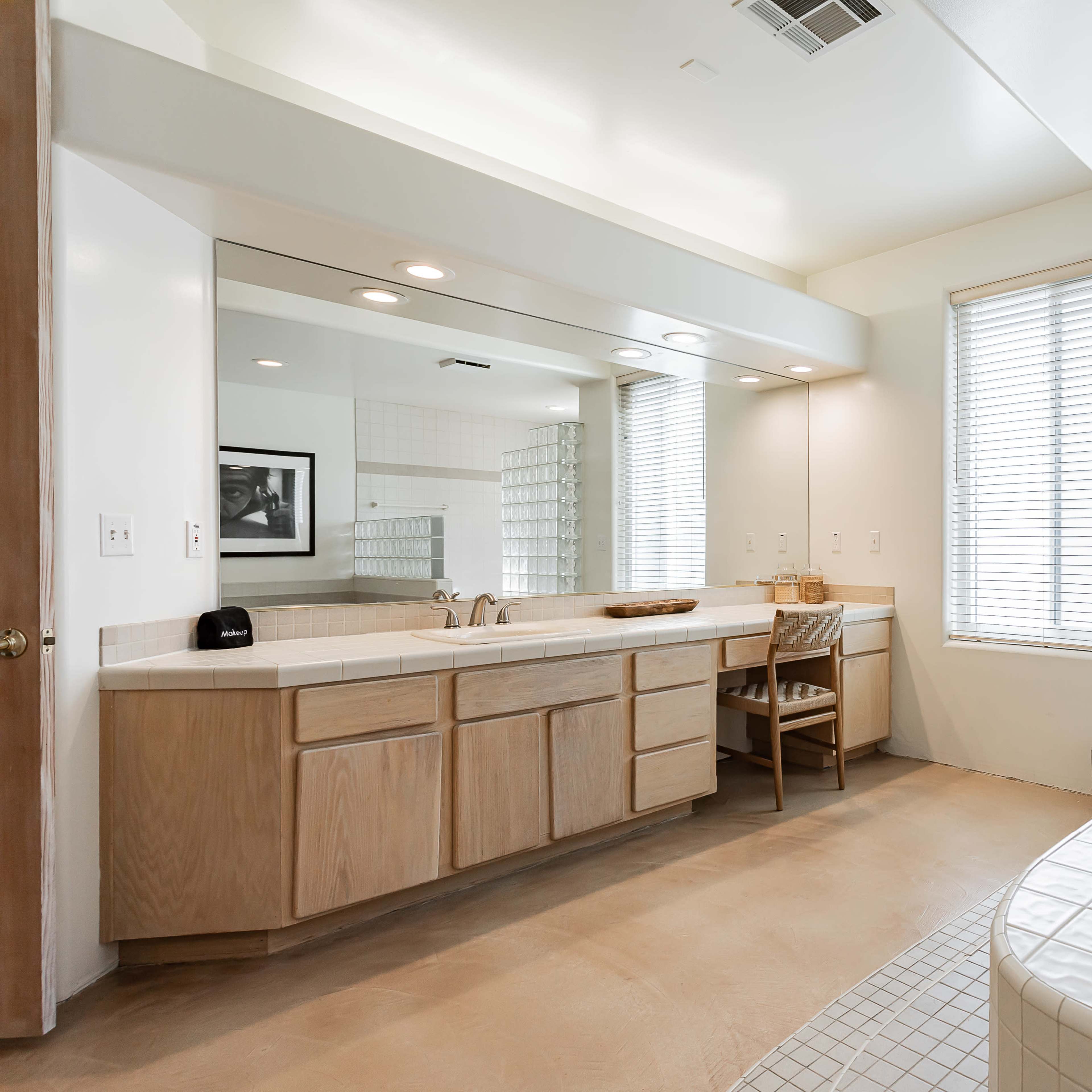 A spacious bathroom featuring a double vanity with a large mirror, a glass block wall for natural light, and a jetted bathtub.