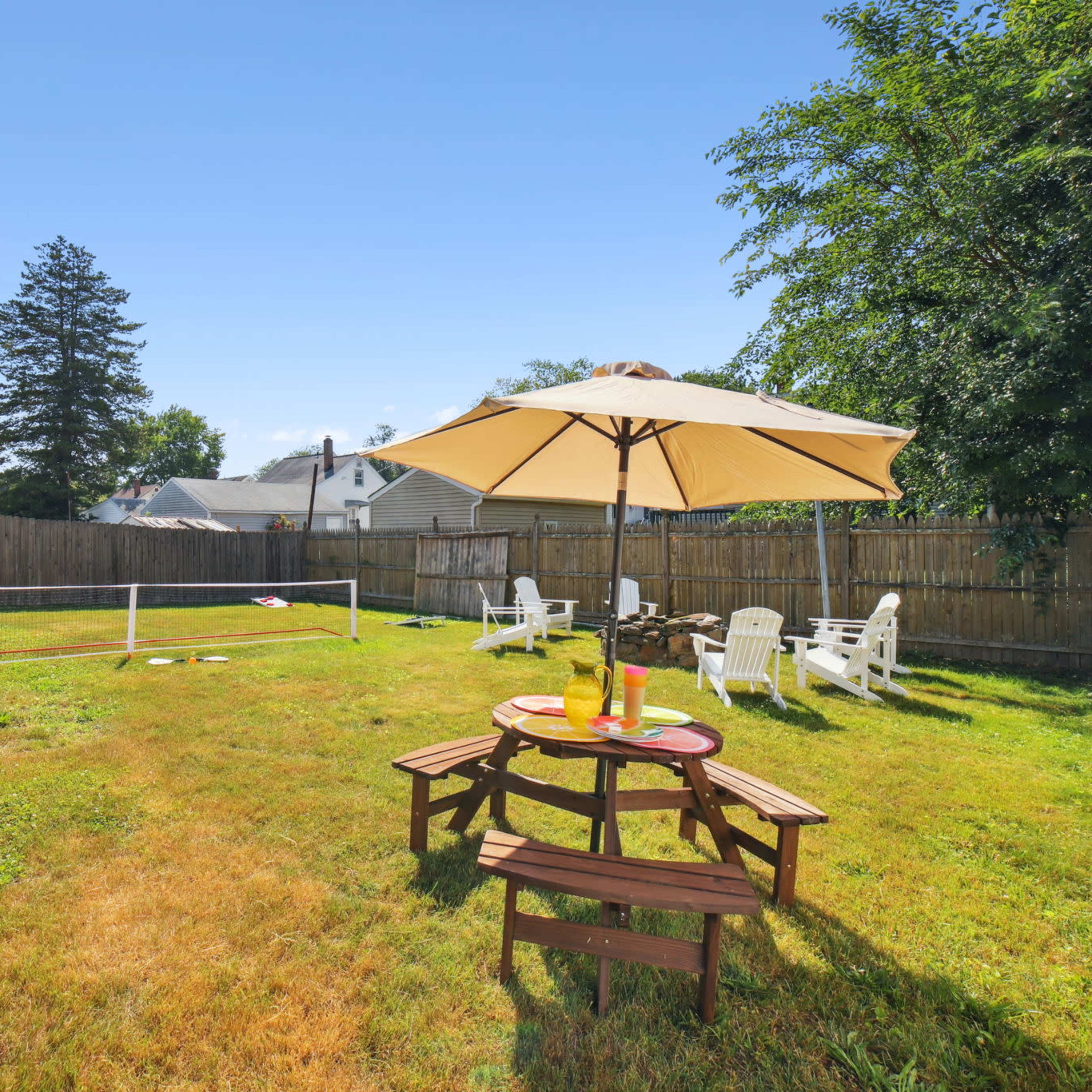 A grassy backyard with a volleyball net, an umbrella-covered table, and white lawn chairs.