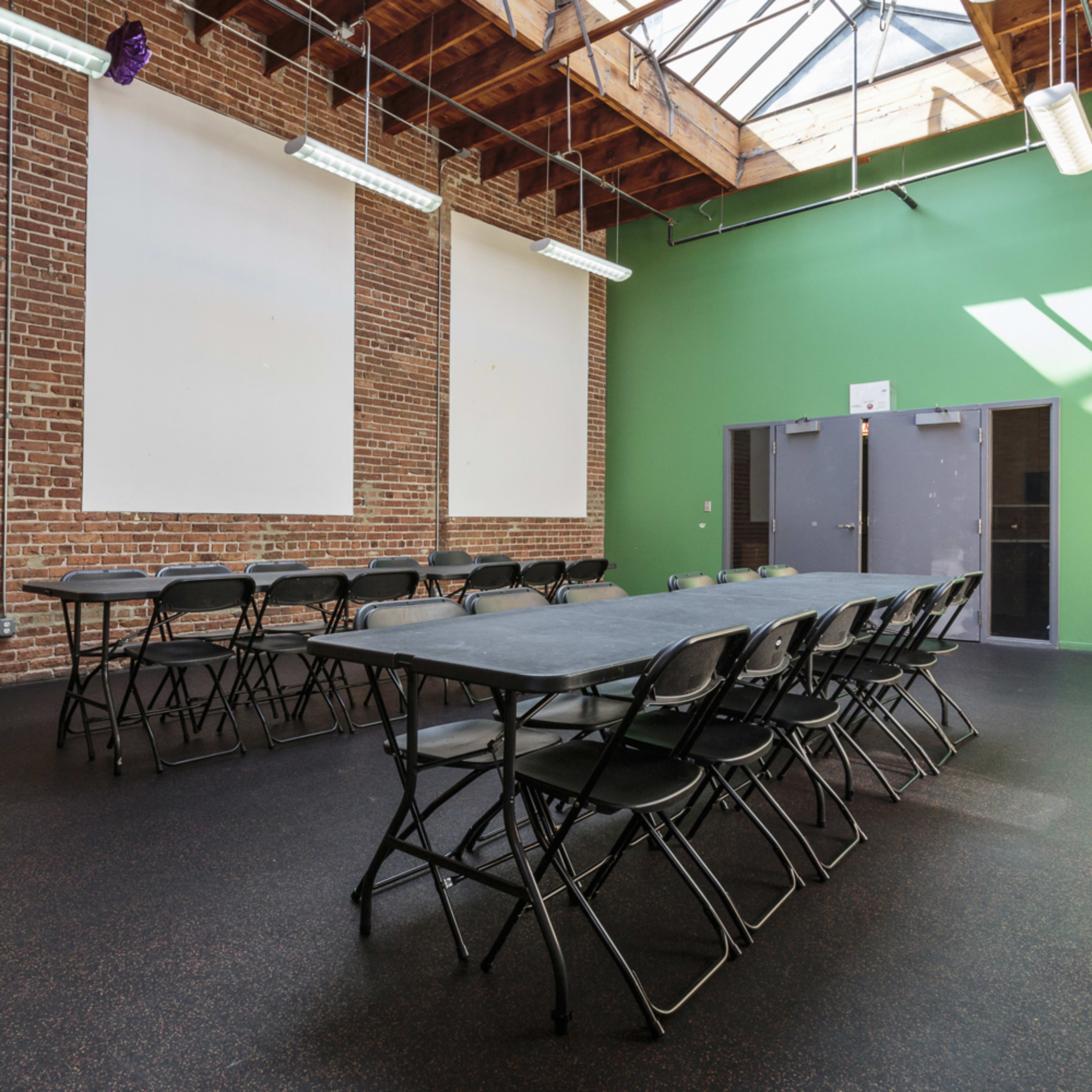 A spacious room with a black floor, green walls, and two long tables set up in a U-shape under a skylight.