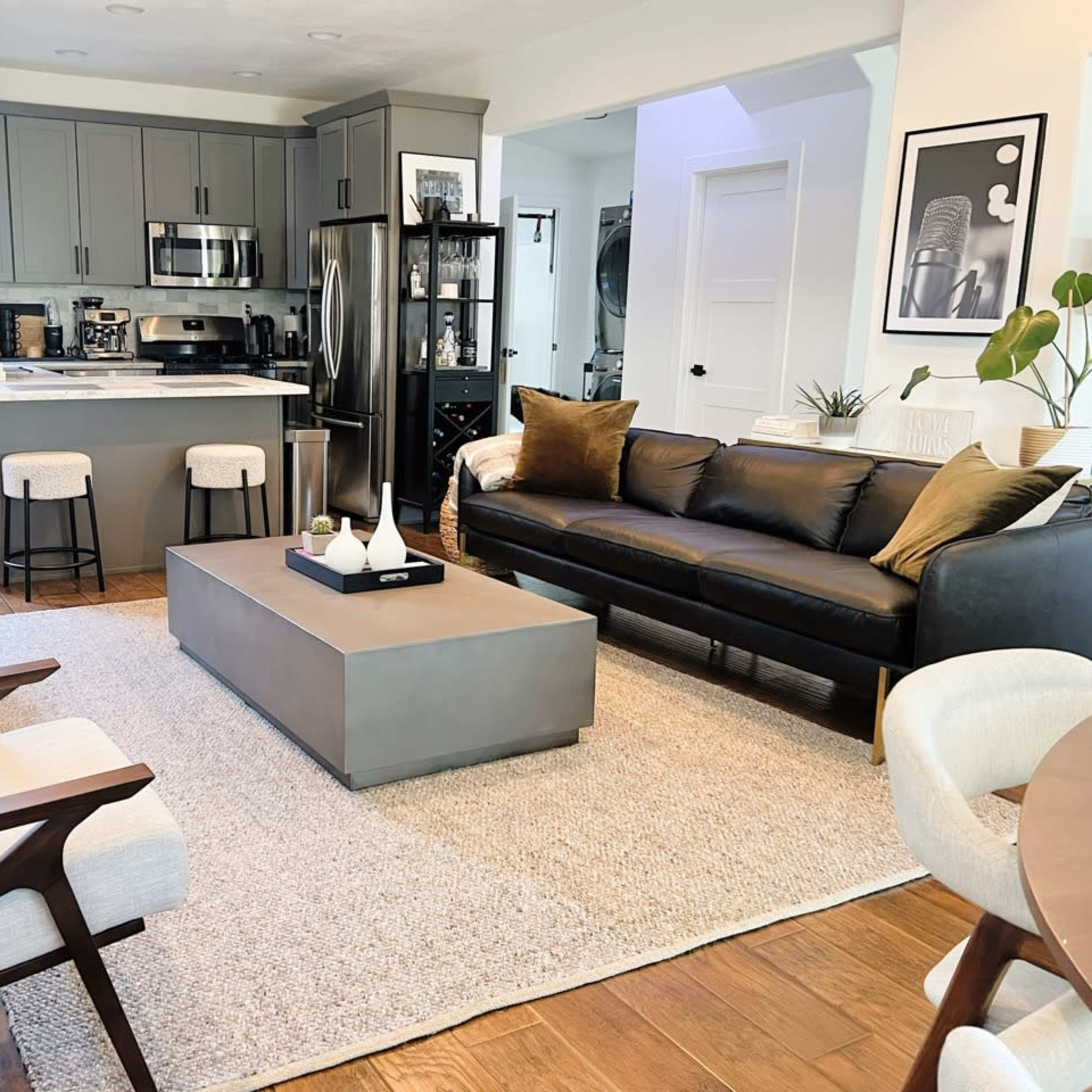 A modern living room with a black sofa, a coffee table in the center, and an open kitchen area in the background.