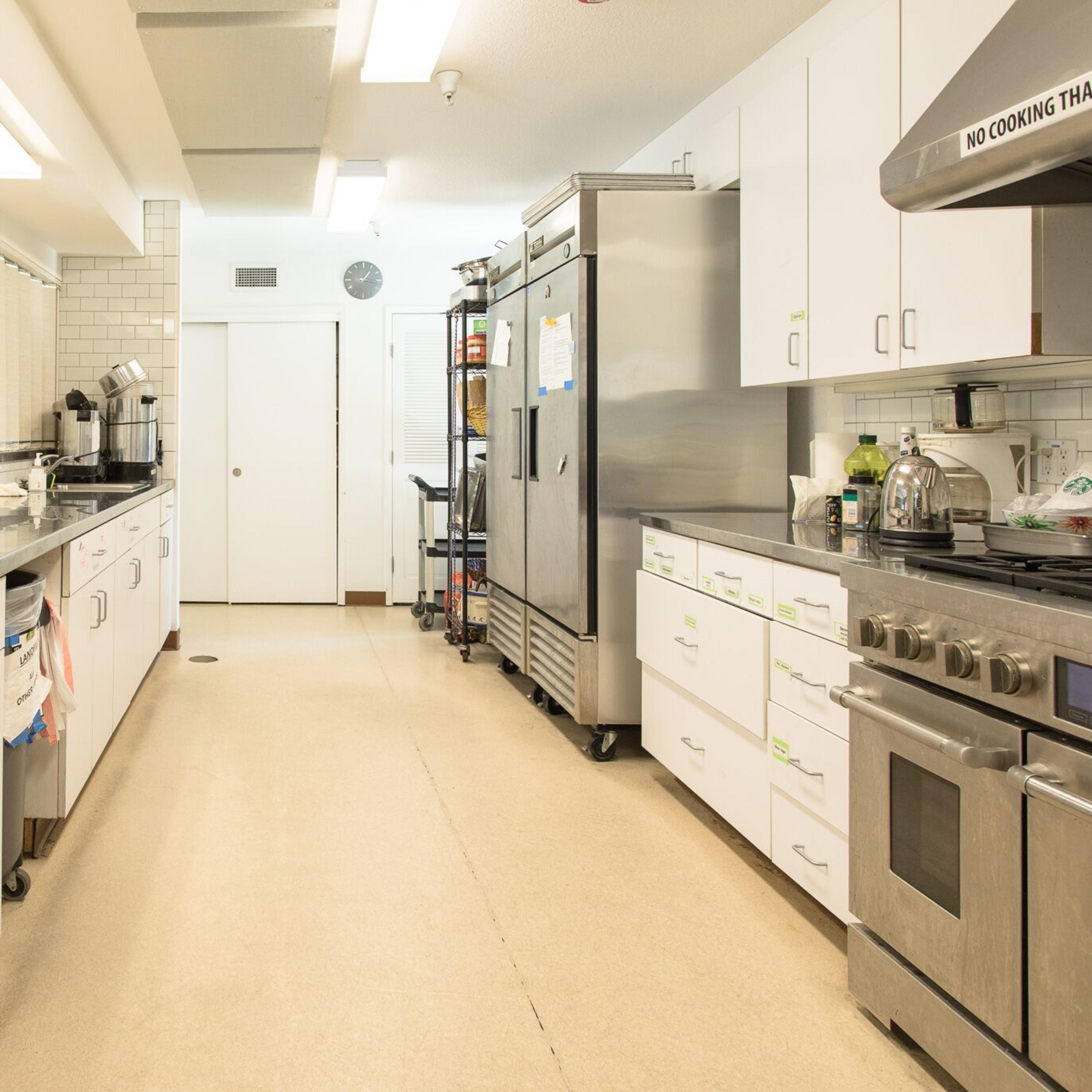 A commercial kitchen with stainless steel appliances, a large sink, and white cabinetry lined along the walls.