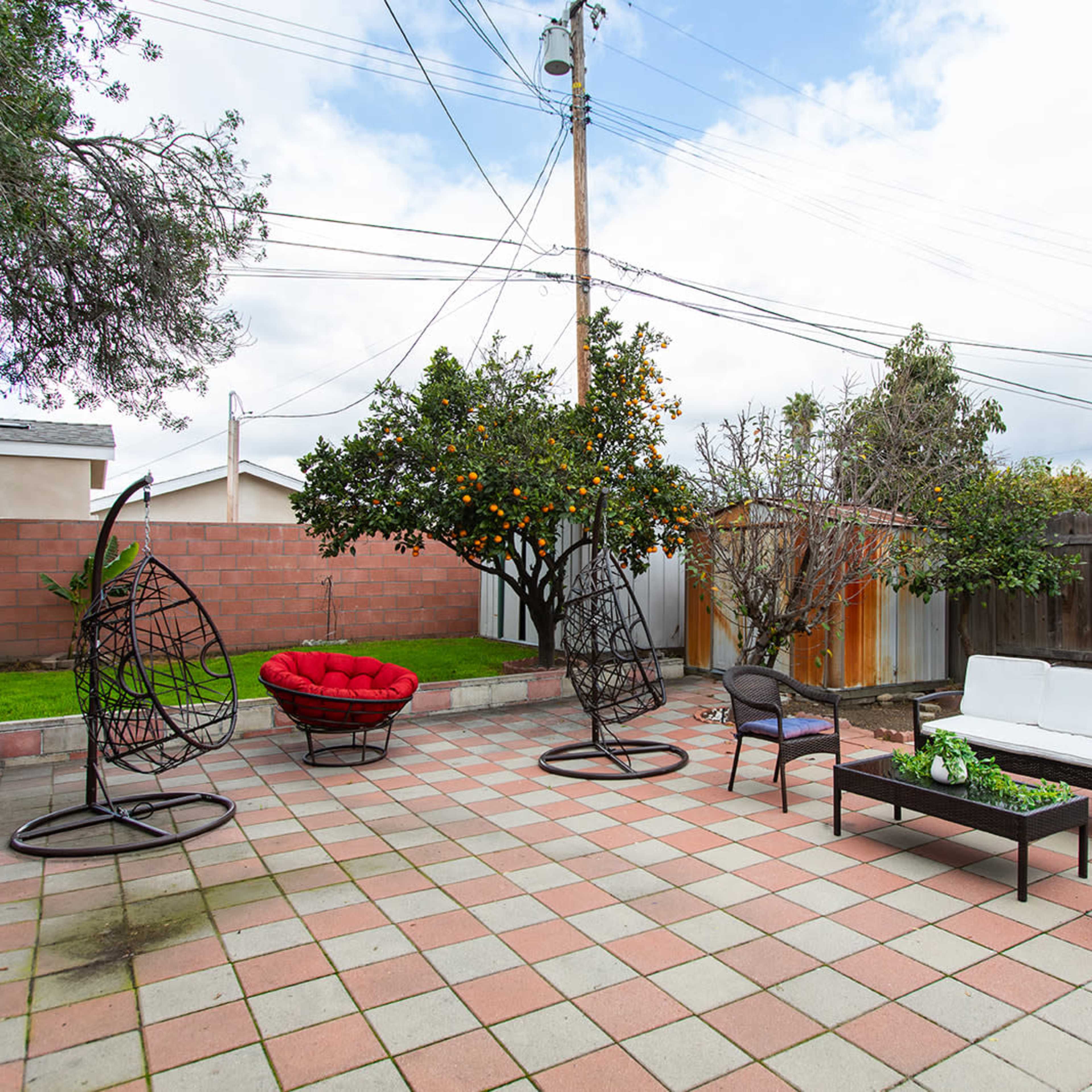 A backyard patio with hanging chairs, a seating area, and a couple of trees, including a citrus tree, surrounded by a tiled floor.