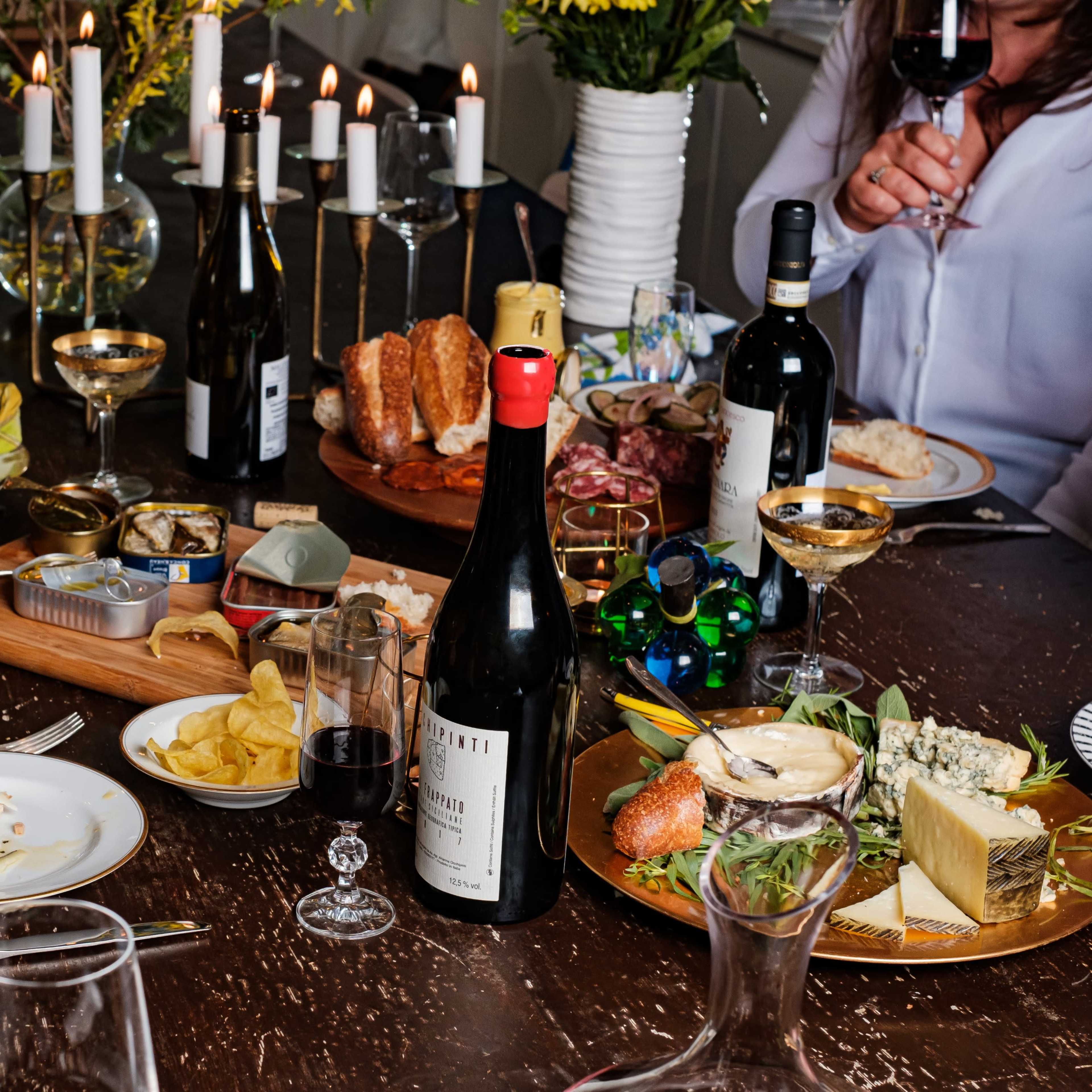 A dining table is set with various dishes, wine bottles, glasses, and candles, as guests enjoy a meal together.