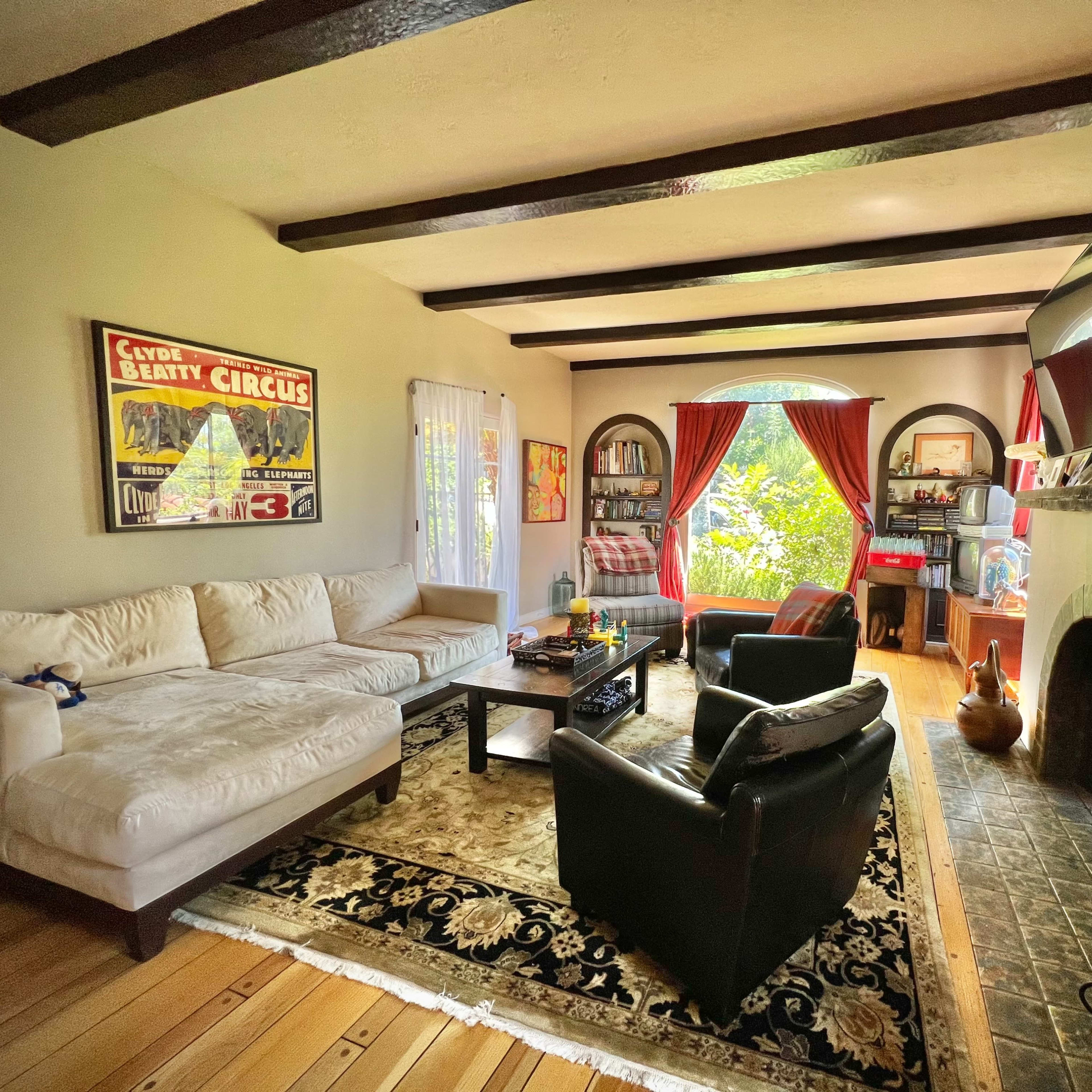 The living room features a sectional sofa, a coffee table, and armchairs arranged around a fireplace, with large windows allowing natural light to enter.
