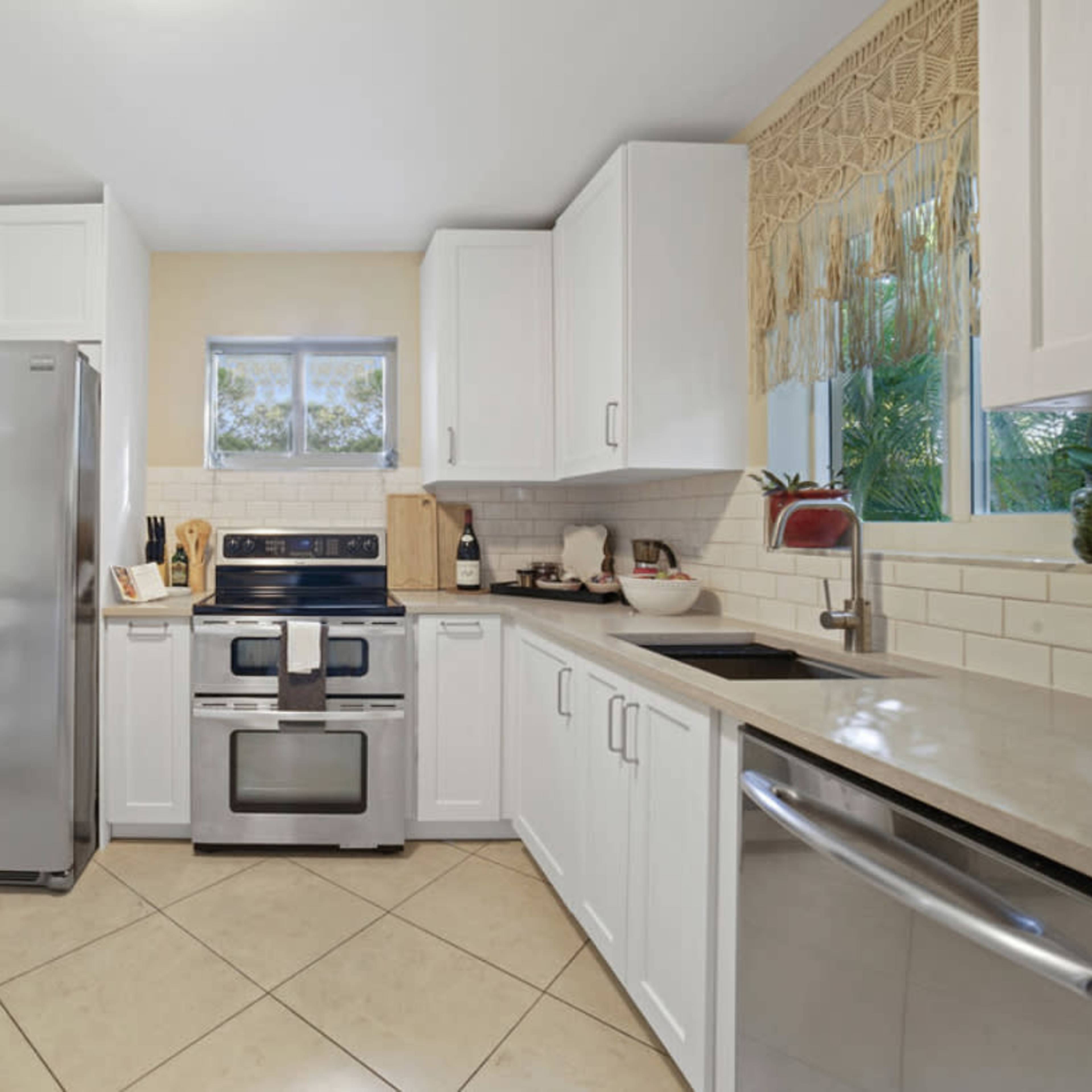 A modern kitchen features stainless steel appliances, white cabinetry, and a tiled floor.