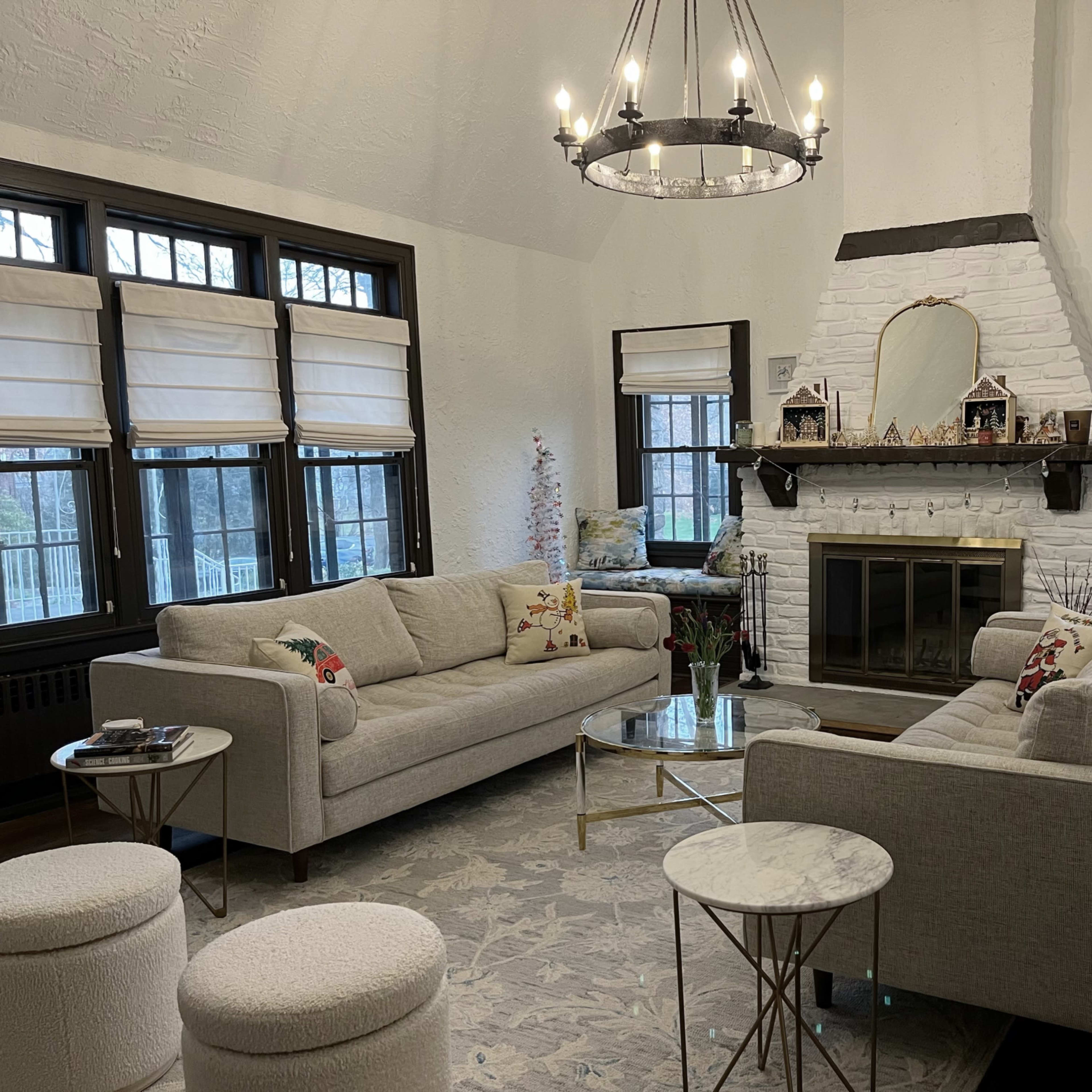 A cozy living room with two sofas facing each other, a fireplace in the center adorned with decorative items, and large windows letting in natural light.