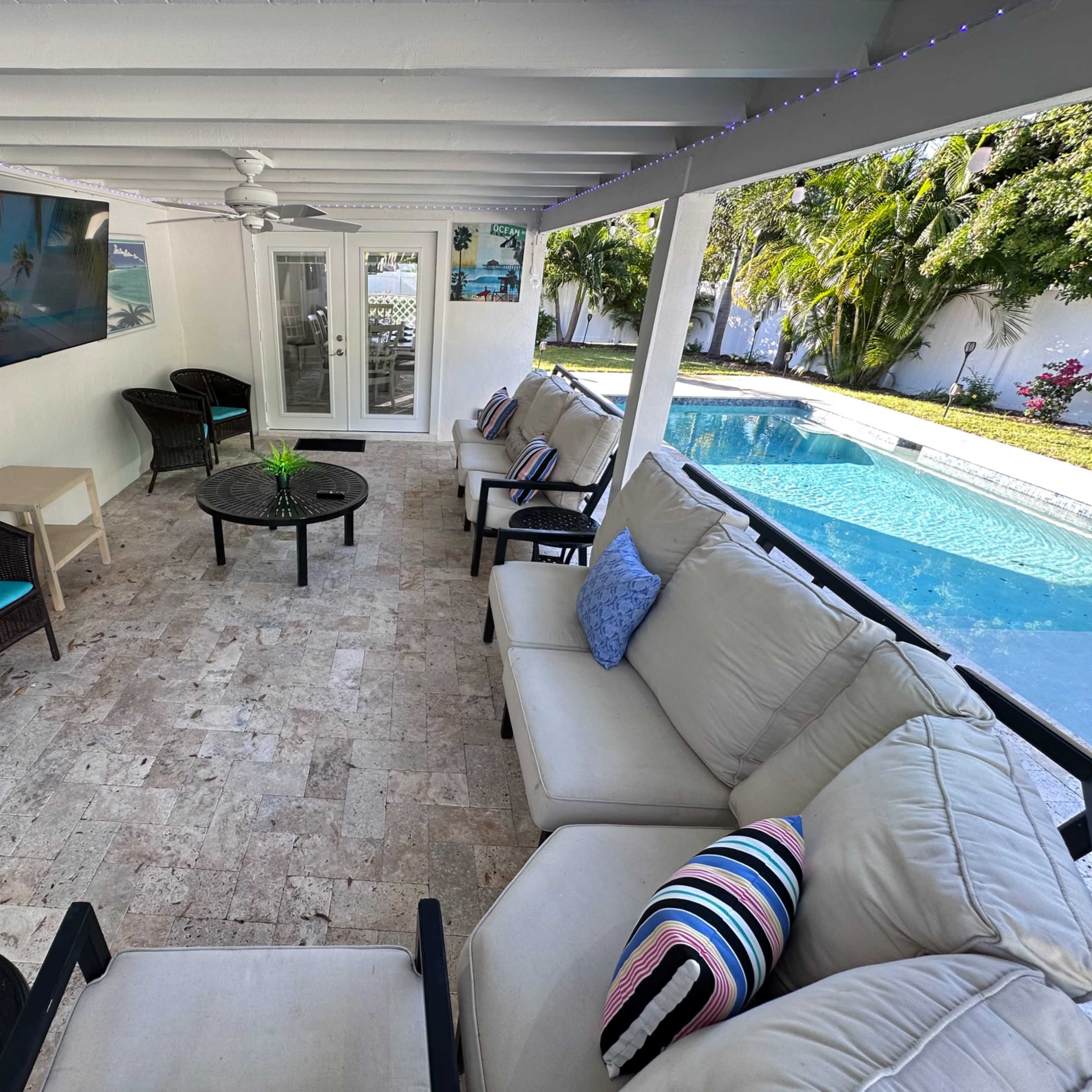 A covered patio area with seating and a view of a swimming pool in the background.