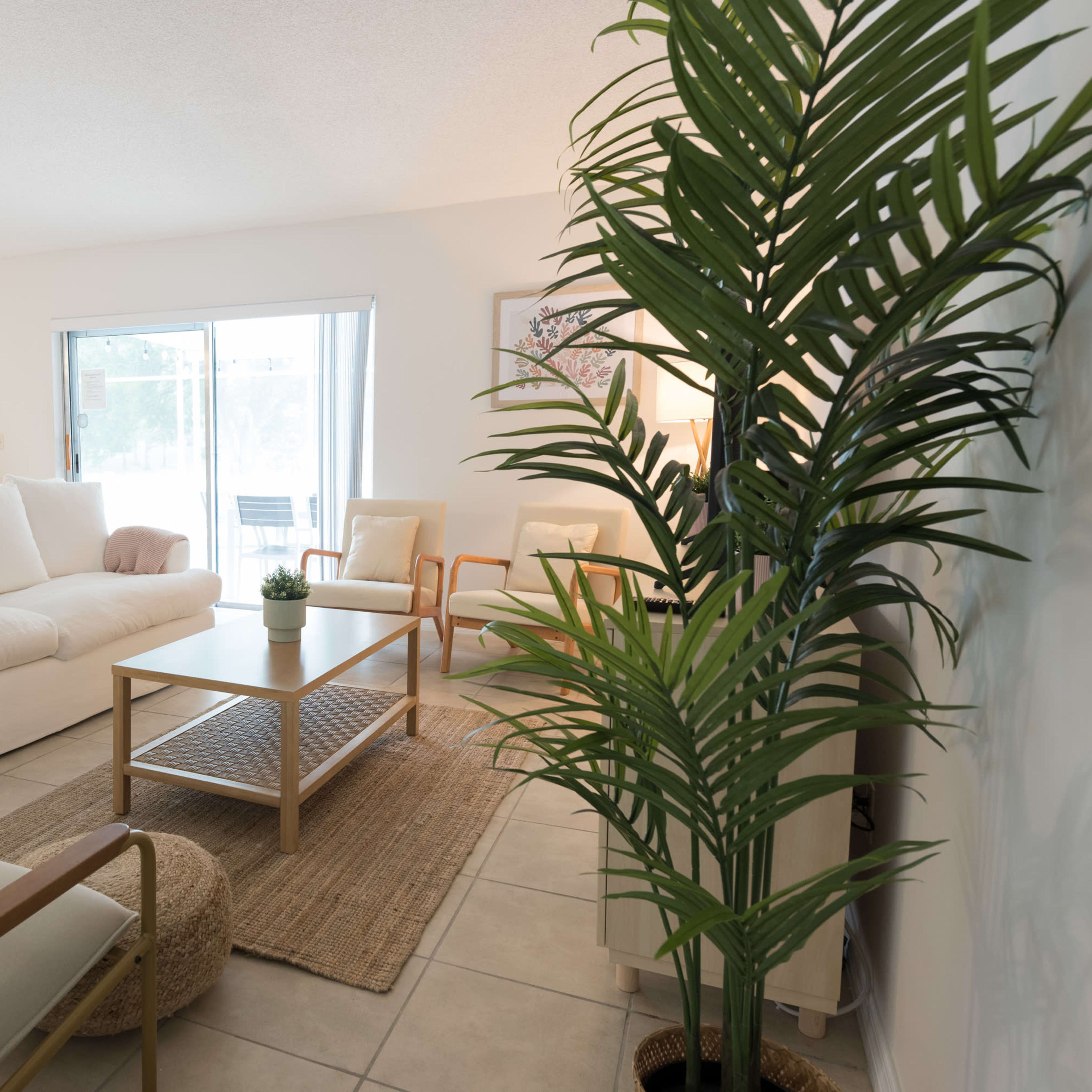 A modern living room with a white sectional sofa, a wooden coffee table on a woven rug, and large windows providing natural light.