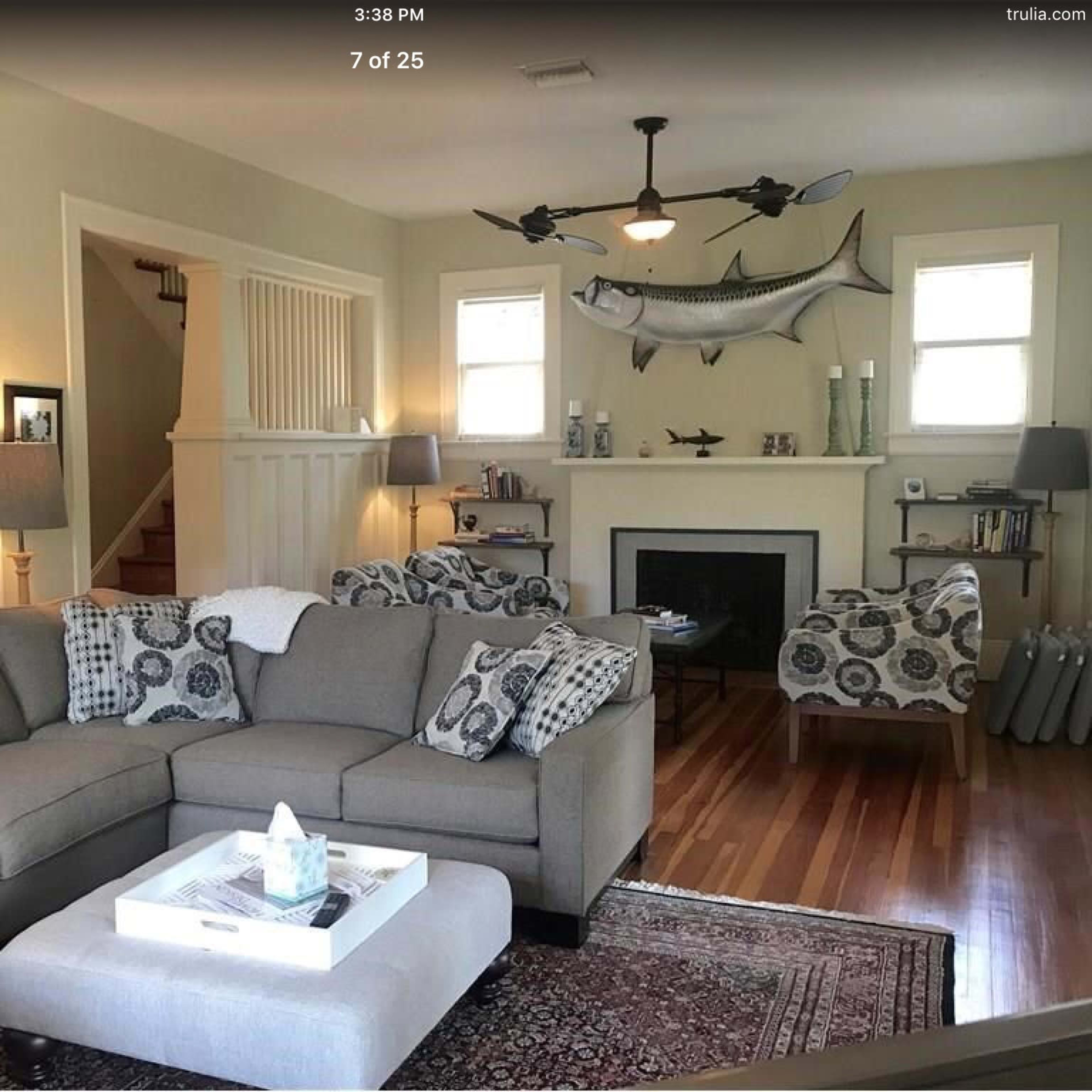 The living room features a gray sectional sofa, two patterned chairs, and a fireplace with a mounted fish decoration on the wall.