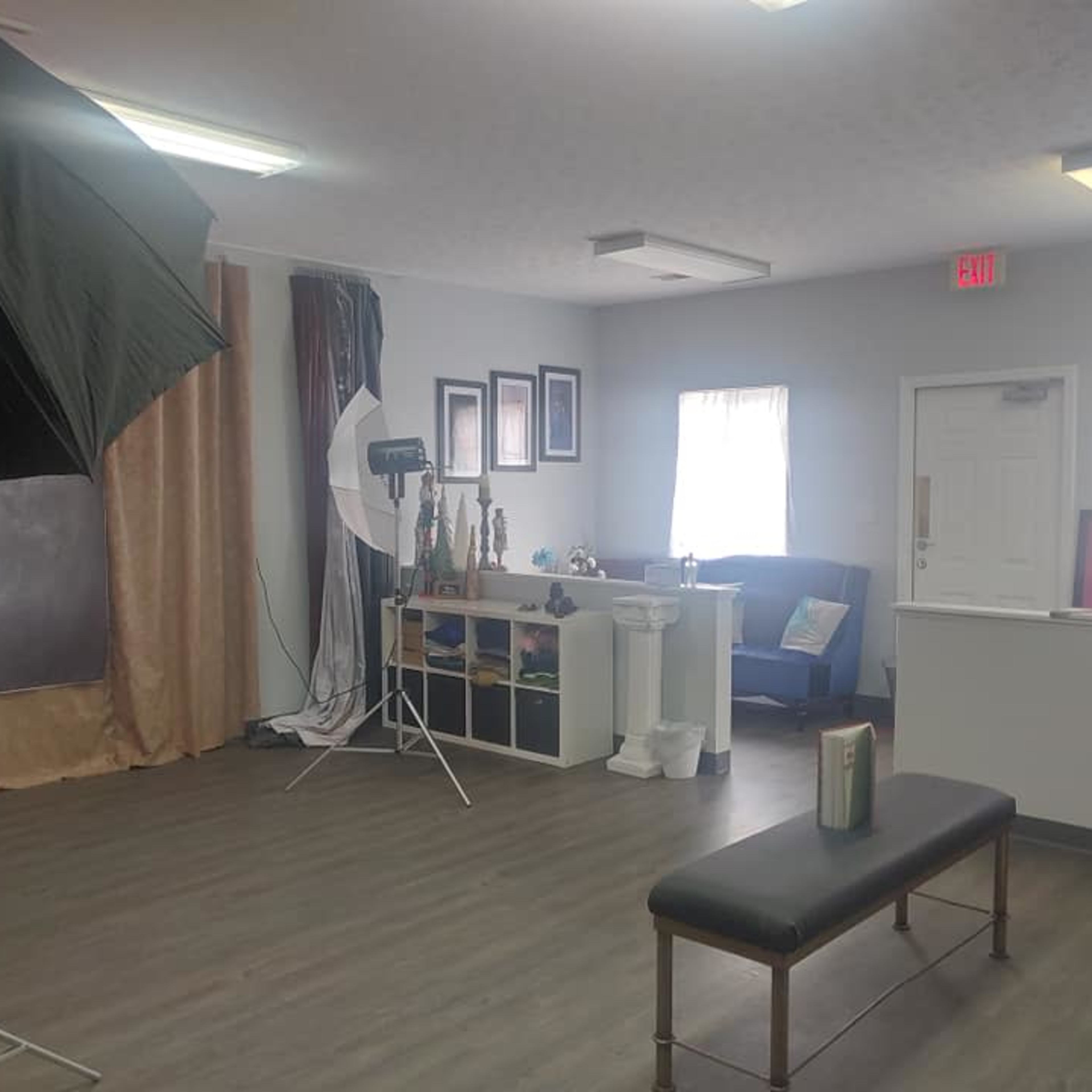 A photography studio with a backdrop, lighting equipment, a bench, and various props arranged on a shelf.