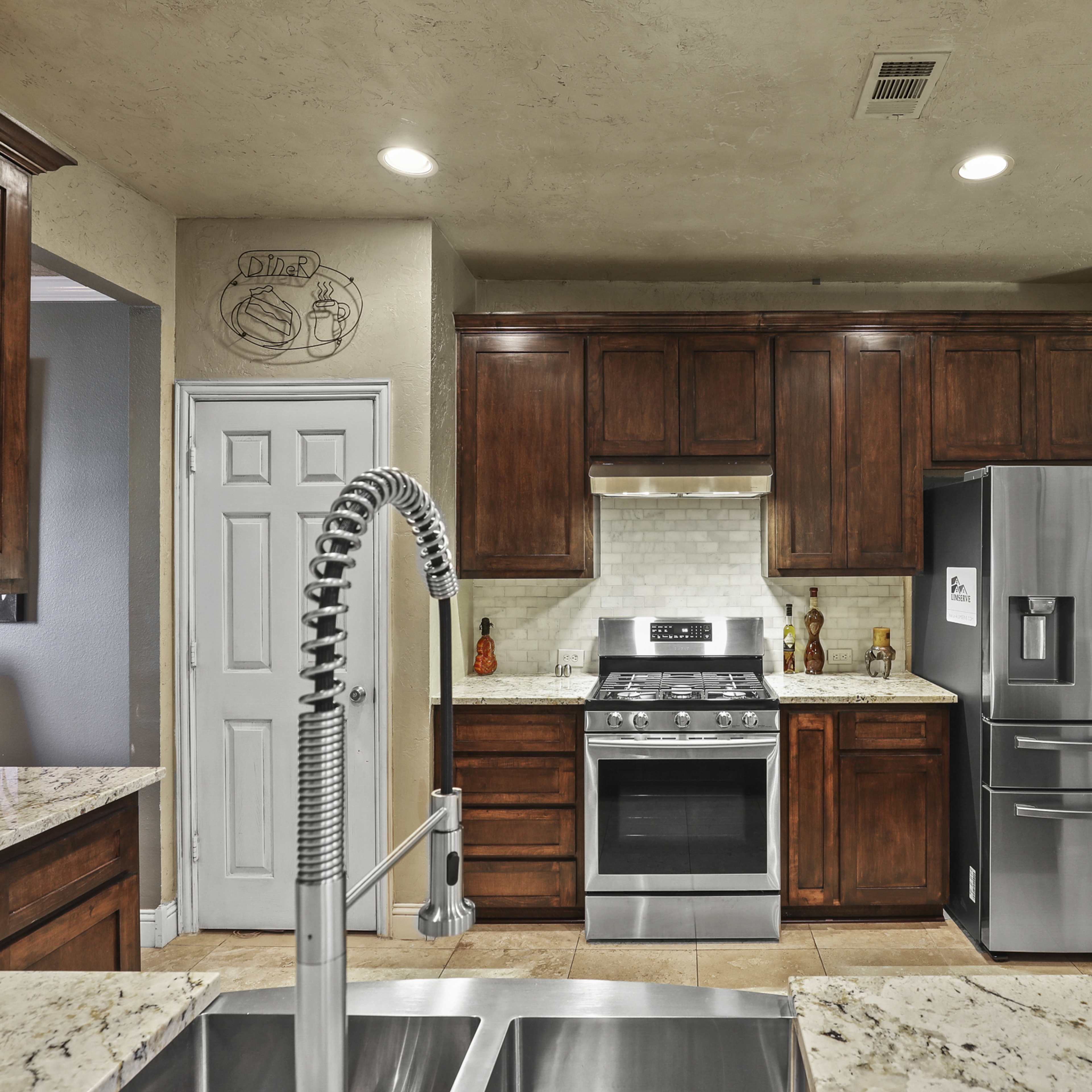 The kitchen features dark wooden cabinets, granite countertops, stainless steel appliances, and a central island with a double sink.