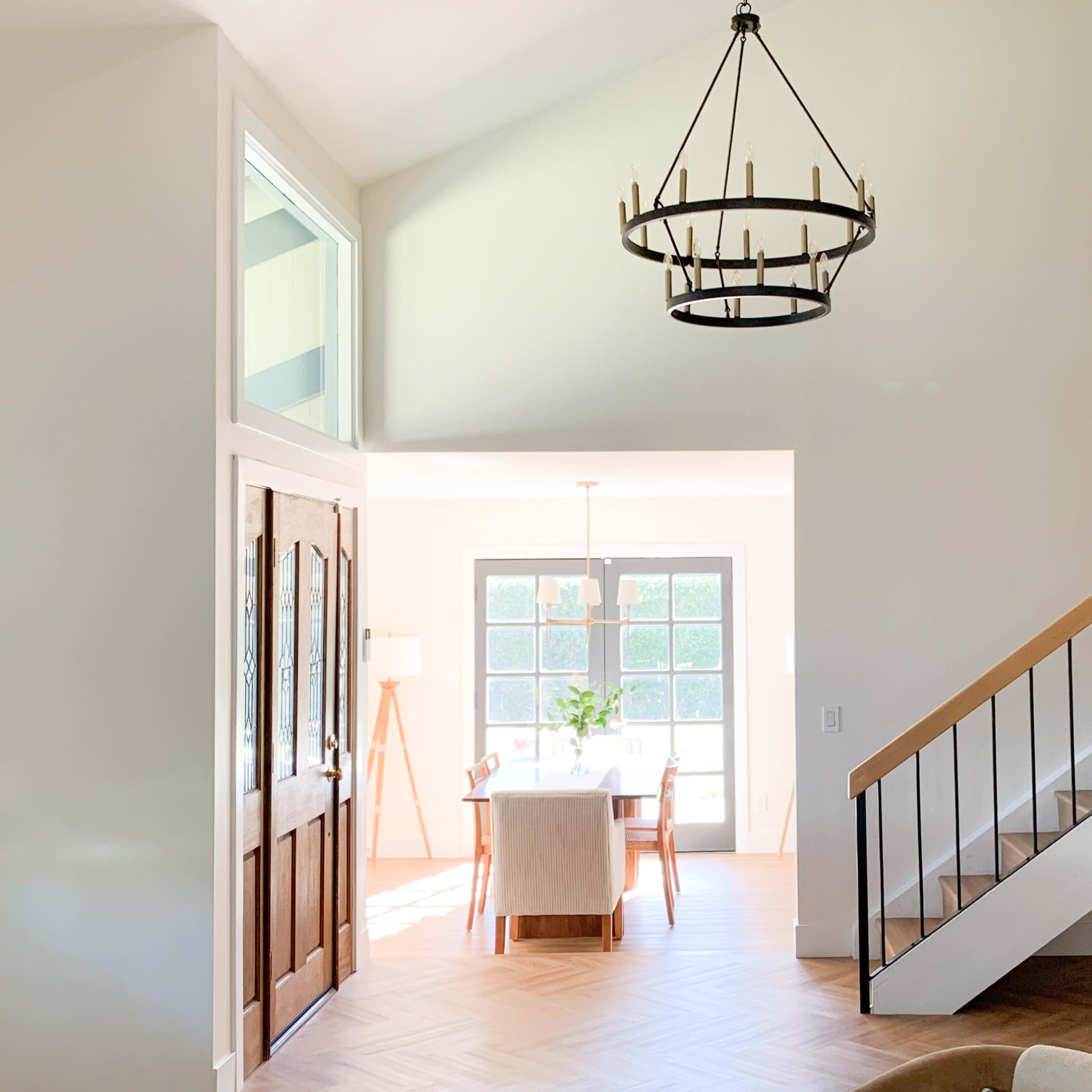 A bright, open interior space with a staircase on the right, a chandelier hanging from the ceiling, and a dining area visible through a doorway.