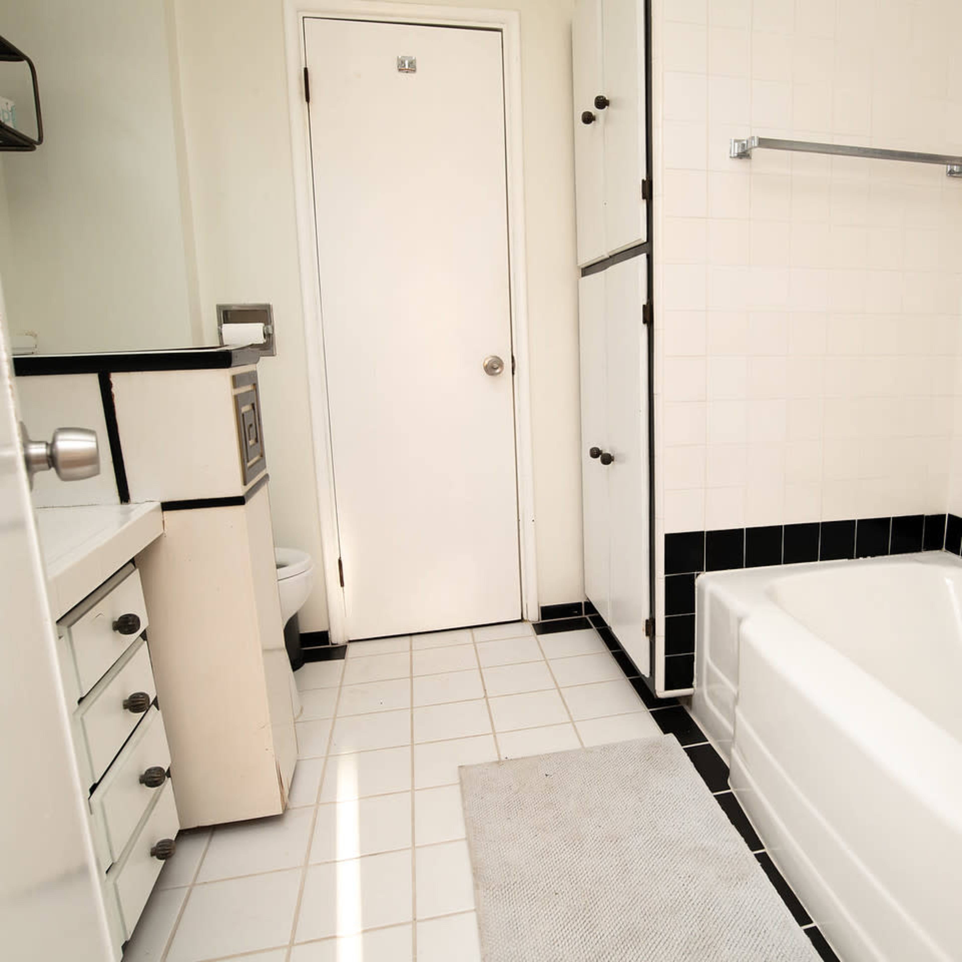 A clean and simple bathroom featuring a bathtub, a toilet, a vanity with storage, and a white tiled floor.