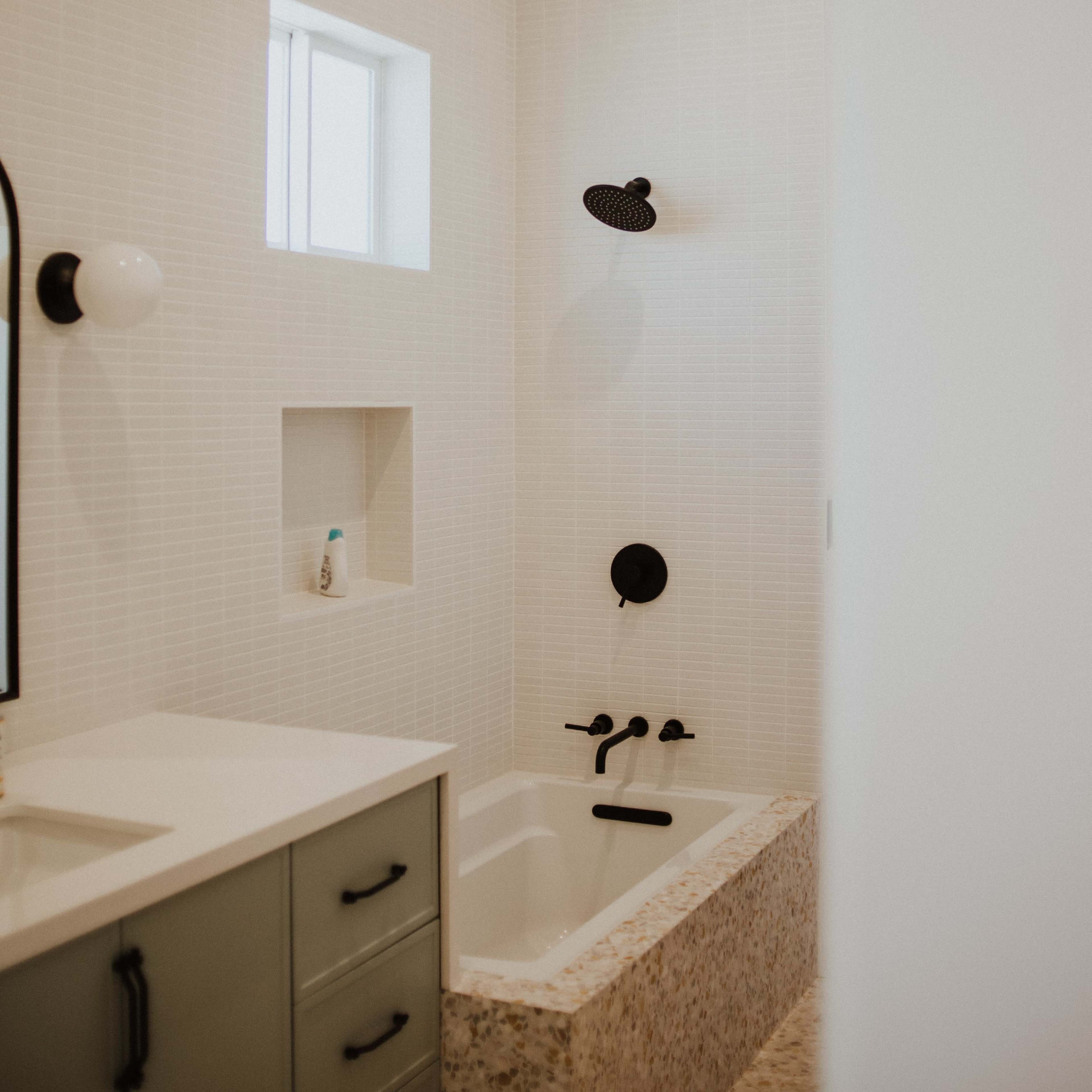 A modern bathroom featuring a bathtub with a shower, a wall-mounted mirror, and built-in shelving.