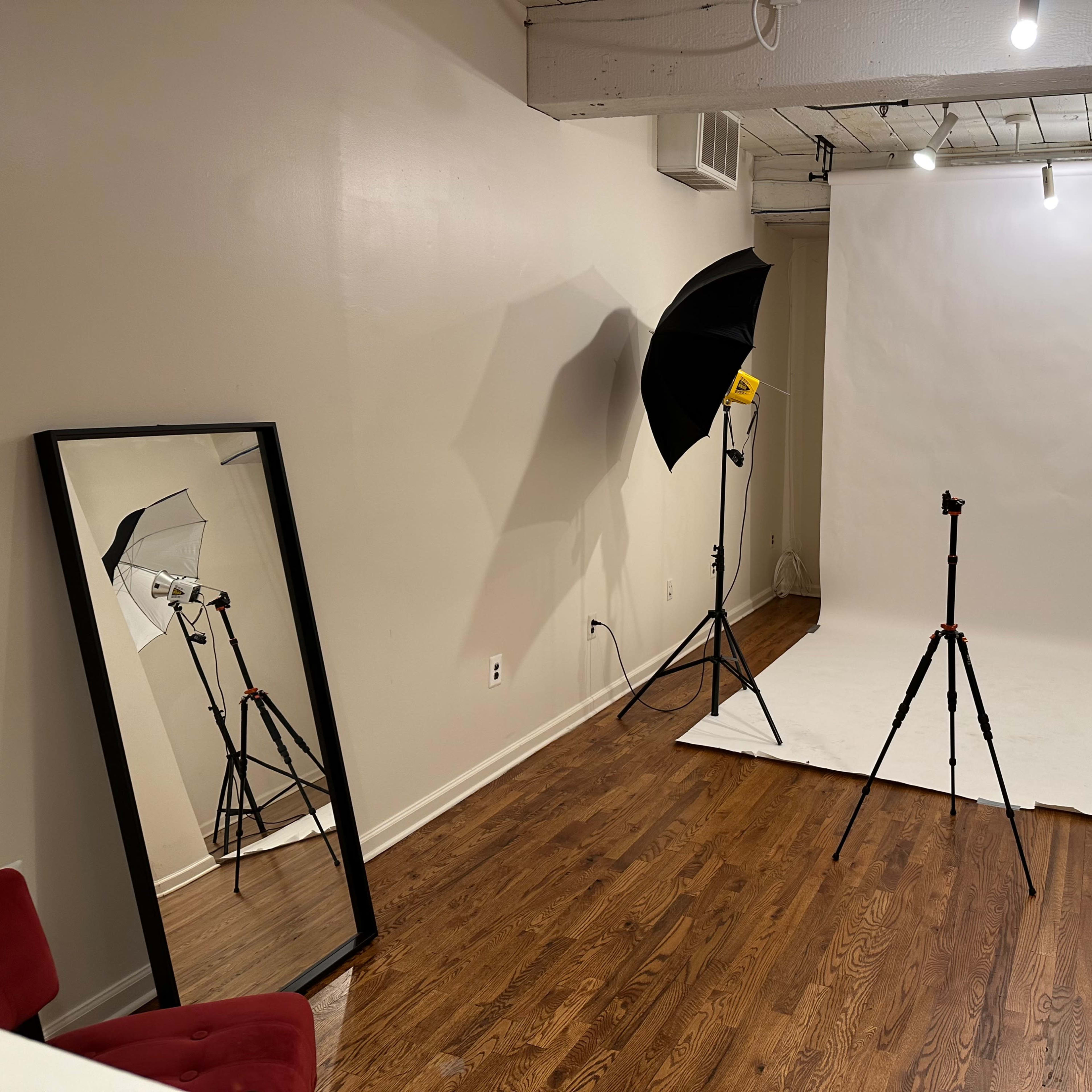 A photography studio with a white backdrop, lighting equipment, and a large mirror reflecting the setup.