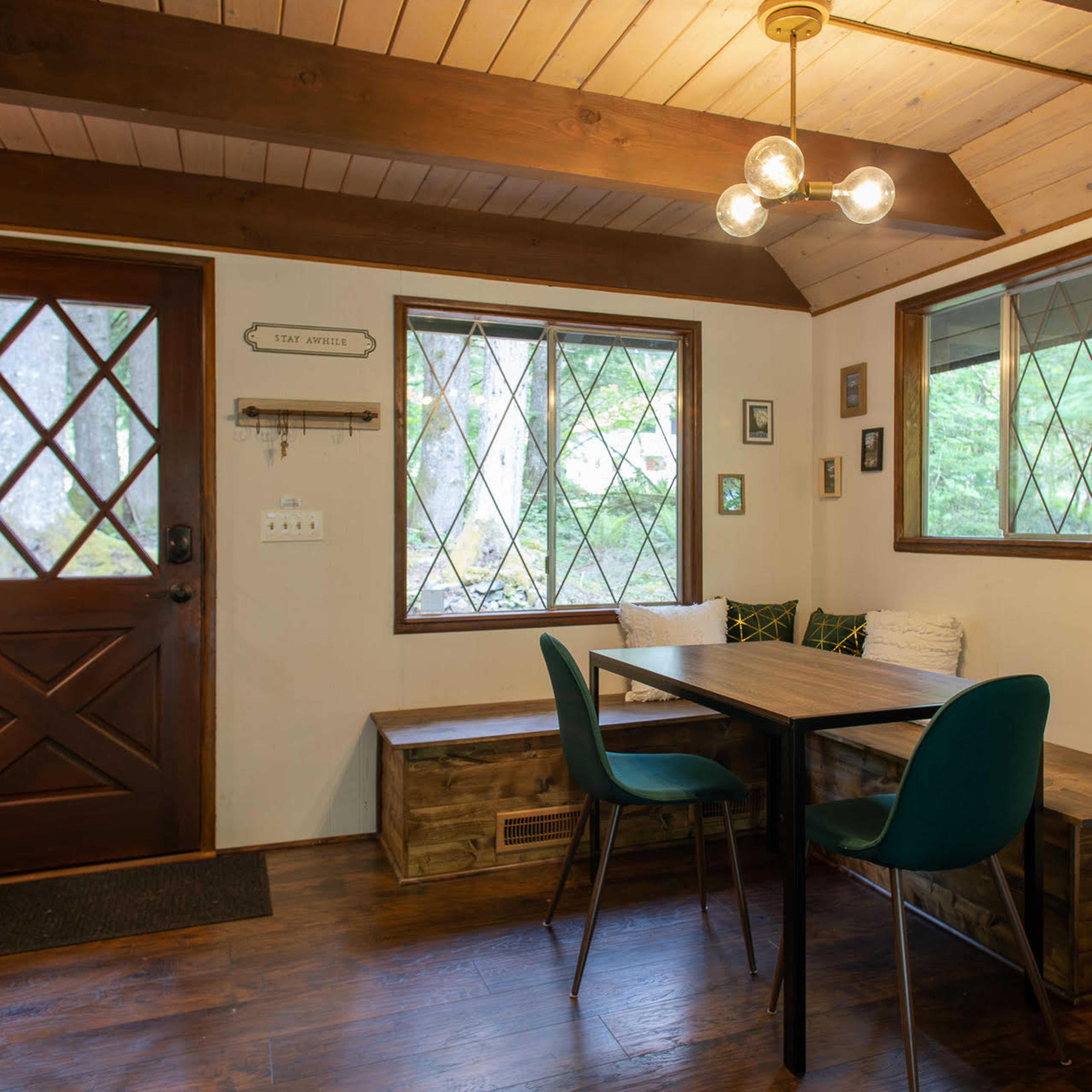 A cozy dining area with a table and green chairs, surrounded by large windows, and a wooden door leading outside.