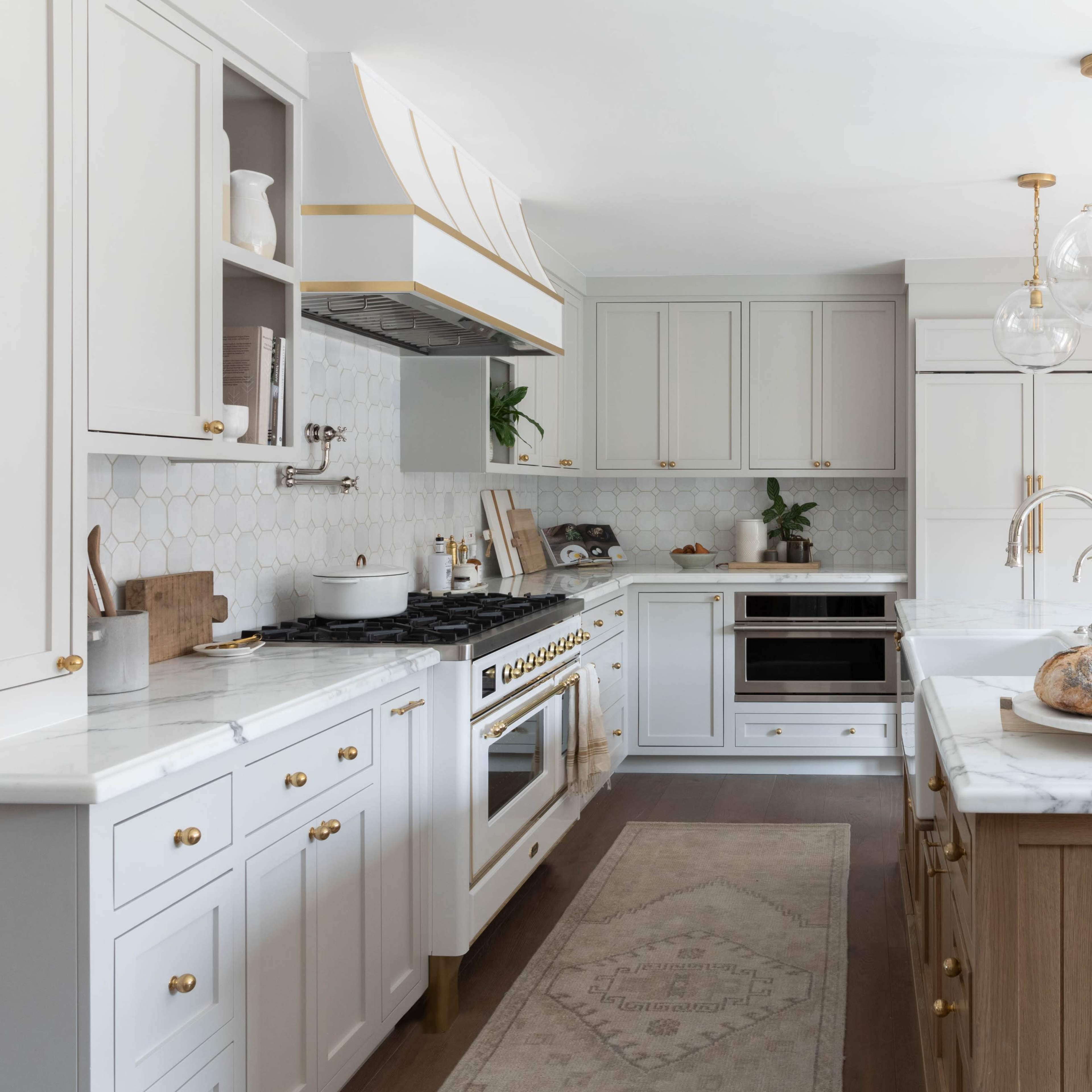 A modern kitchen featuring white cabinetry, a marble countertop, a large oven, and a dining area in the background.