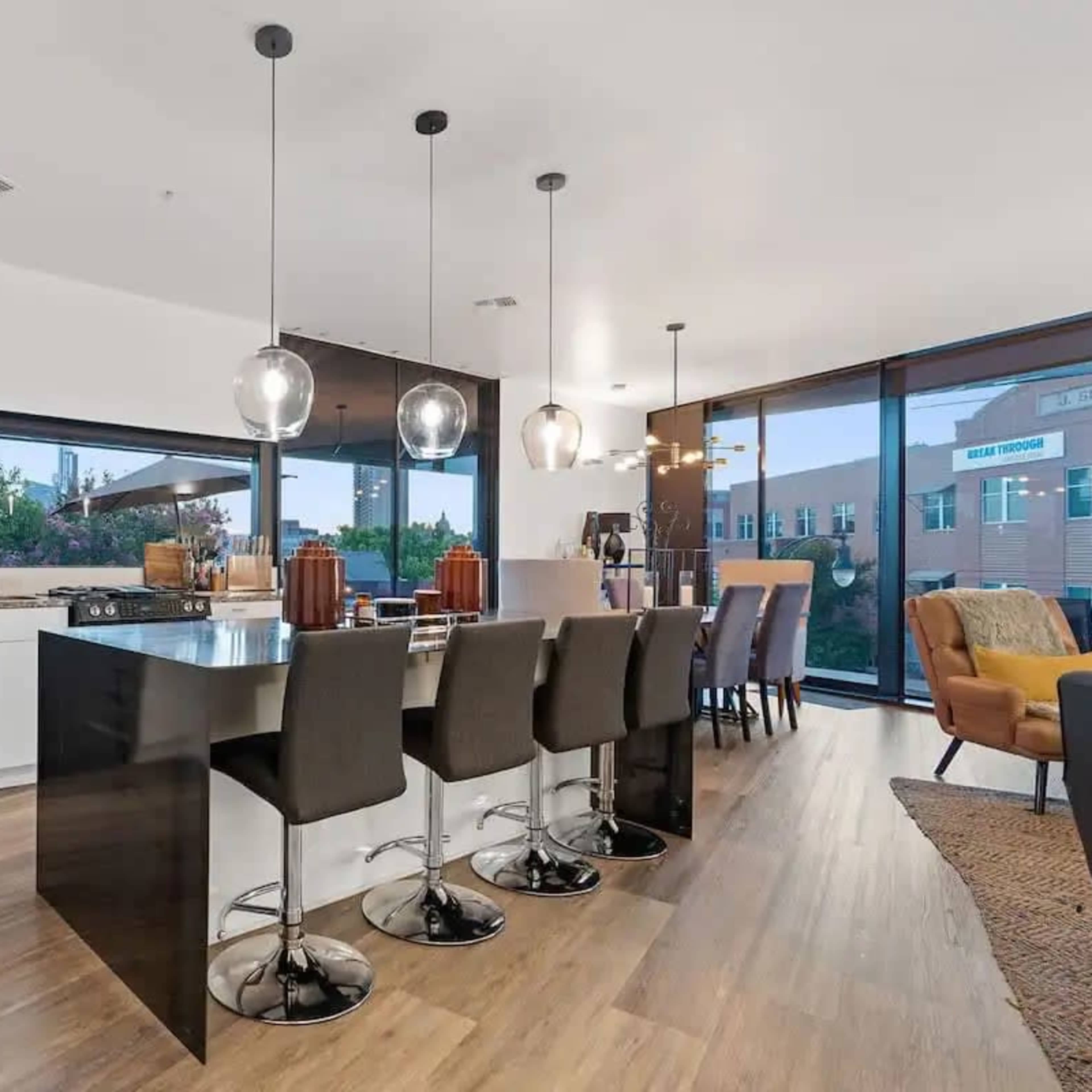 A modern kitchen features sleek black appliances, a central island with seating for four, and large windows showcasing an outdoor view.