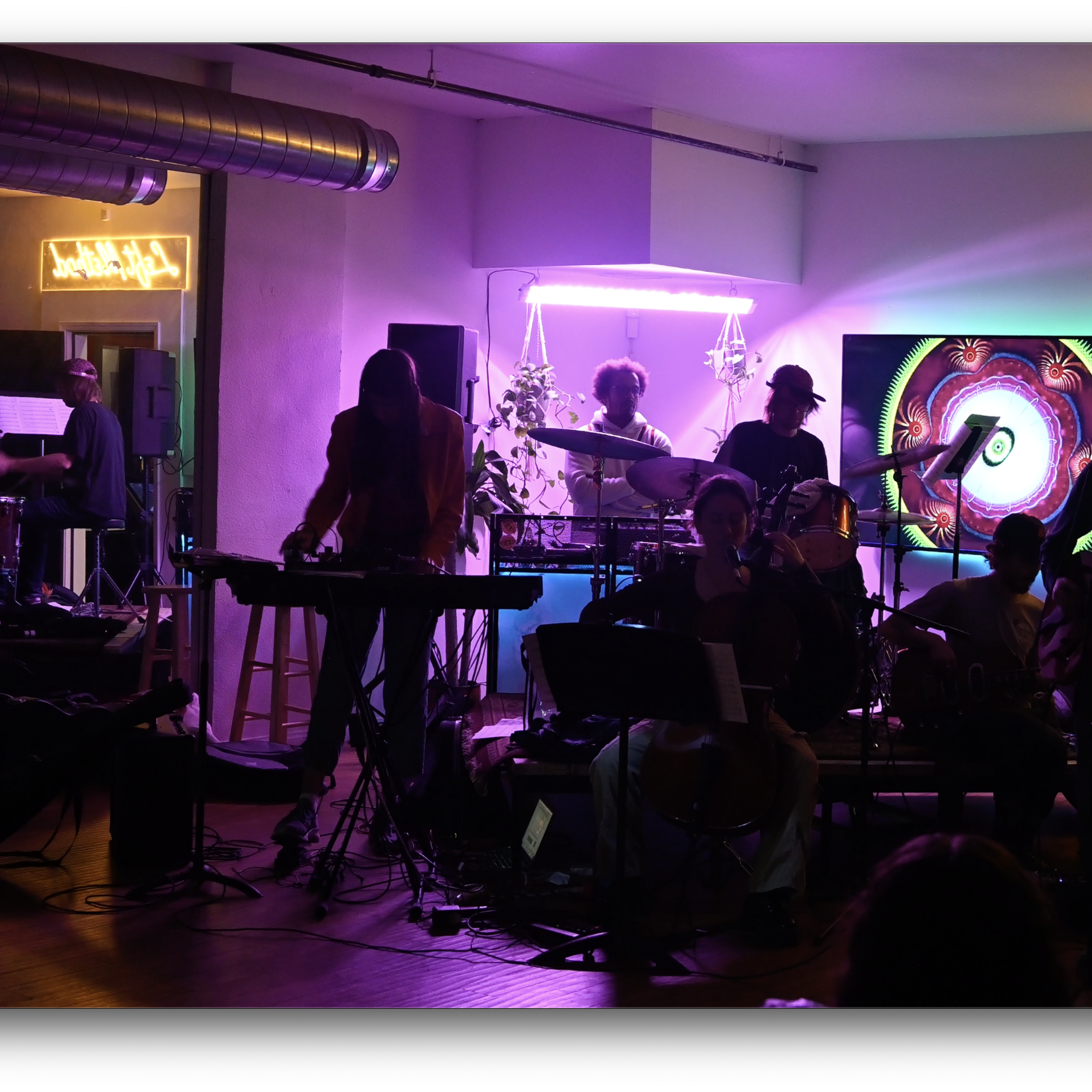 A group of musicians performs on stage in a dimly lit room decorated with neon signs and colorful lighting.