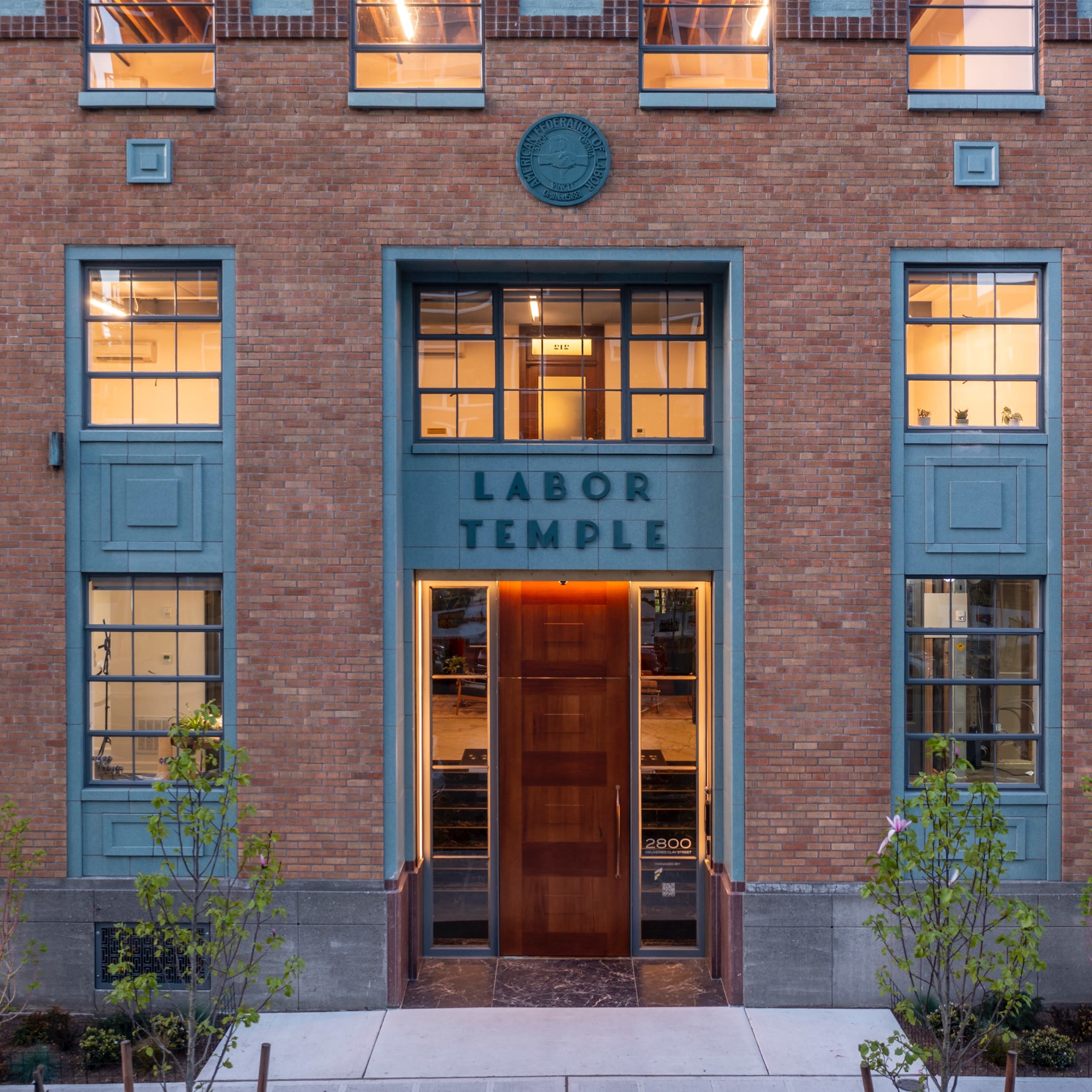 The front facade of a brick building labeled "LABOR TEMPLE," featuring large windows and a wooden entrance door.