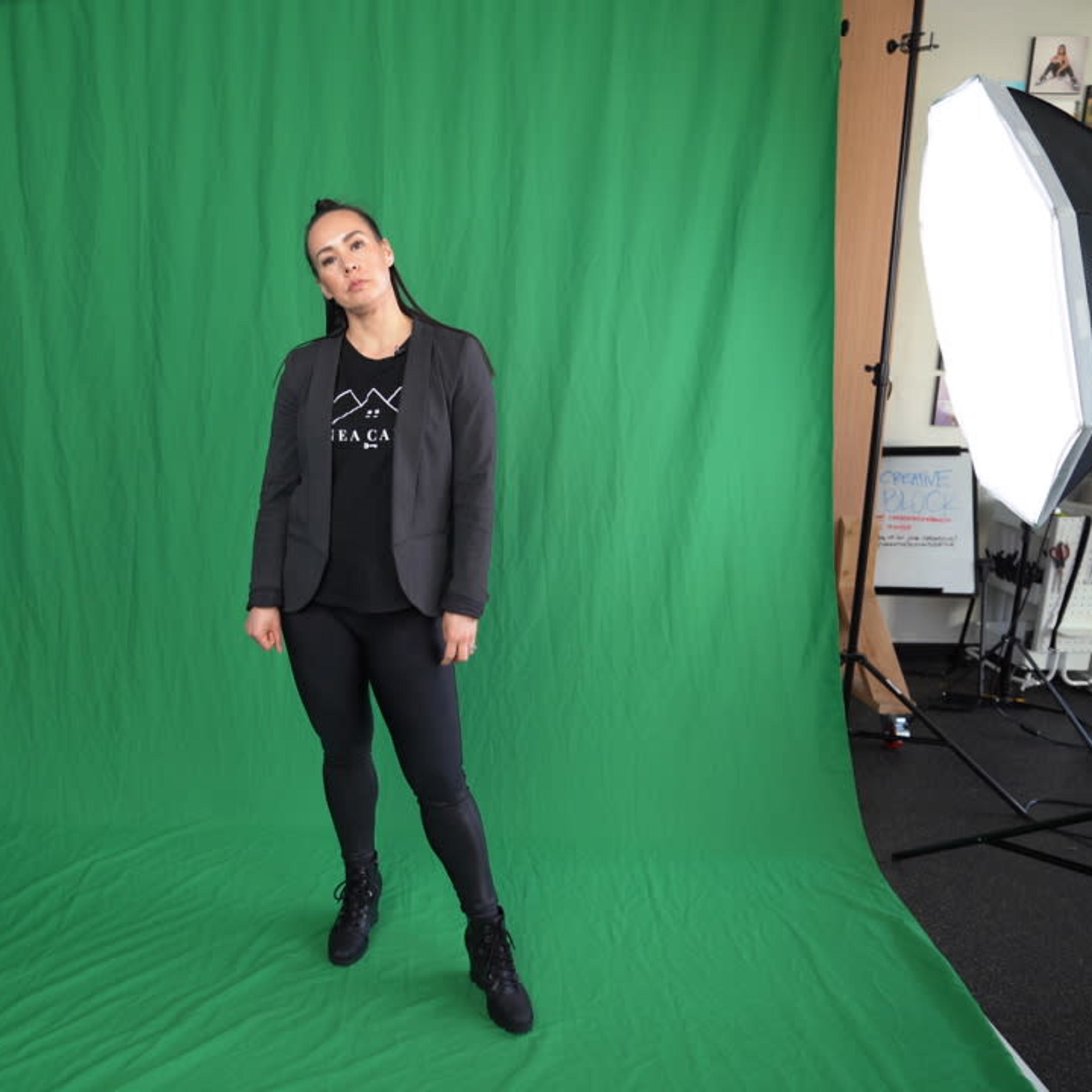 A person stands in front of a green backdrop with studio lights positioned on either side.