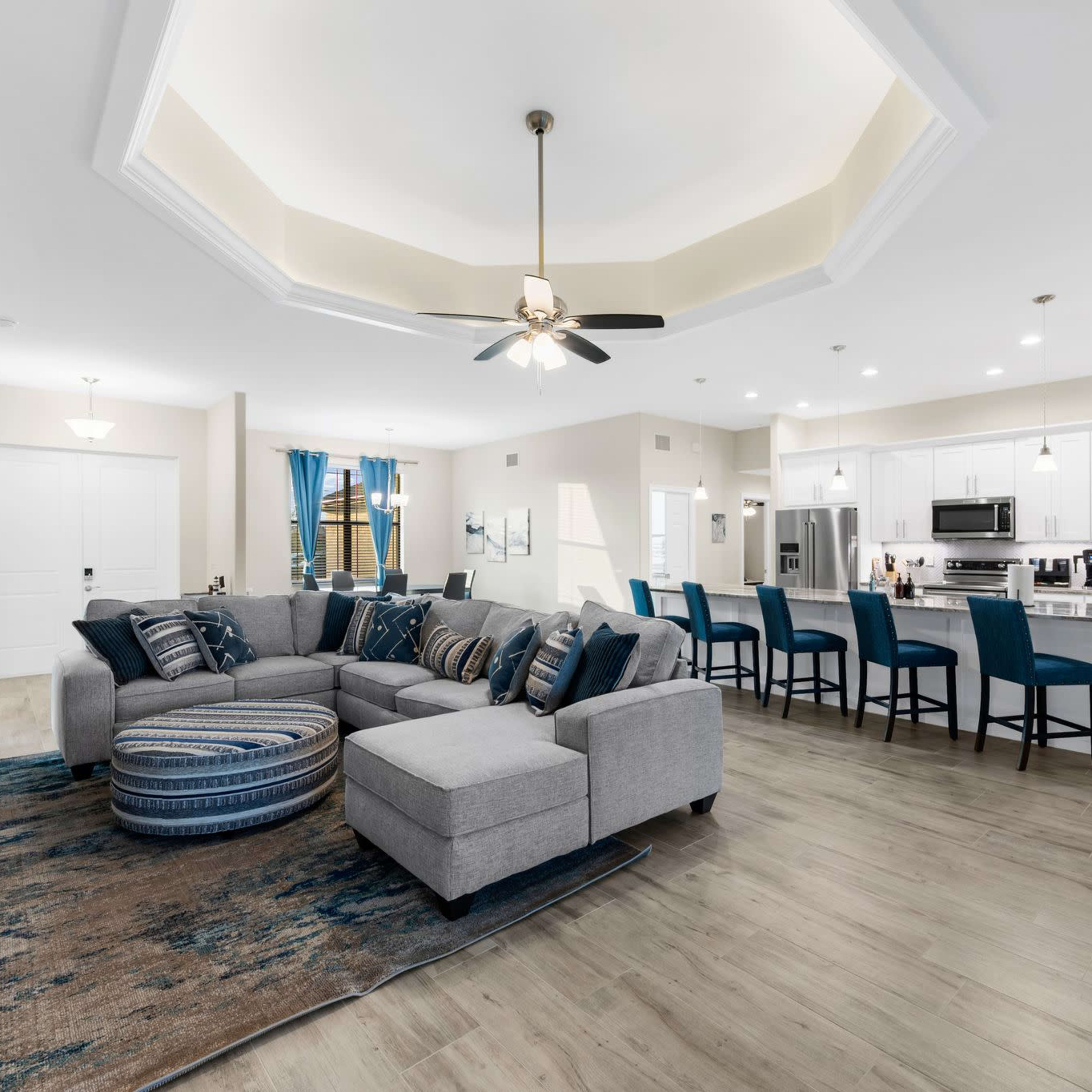 A spacious, modern living area featuring a sectional sofa, accent chairs, and a kitchen bar with high stools.