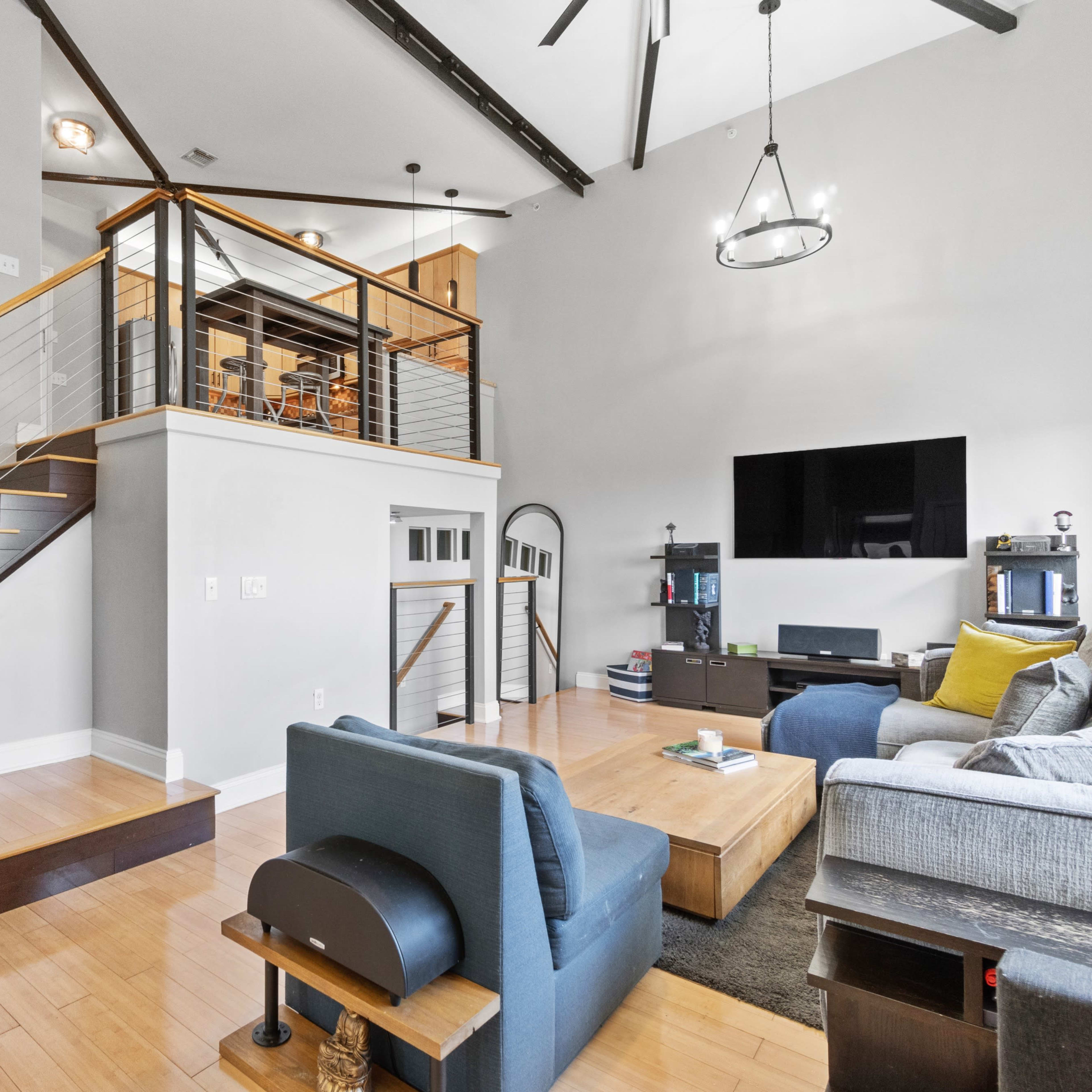 A modern living room with a staircase leading to an upper level, featuring a large coffee table and a sectional sofa with a television mounted on the wall.