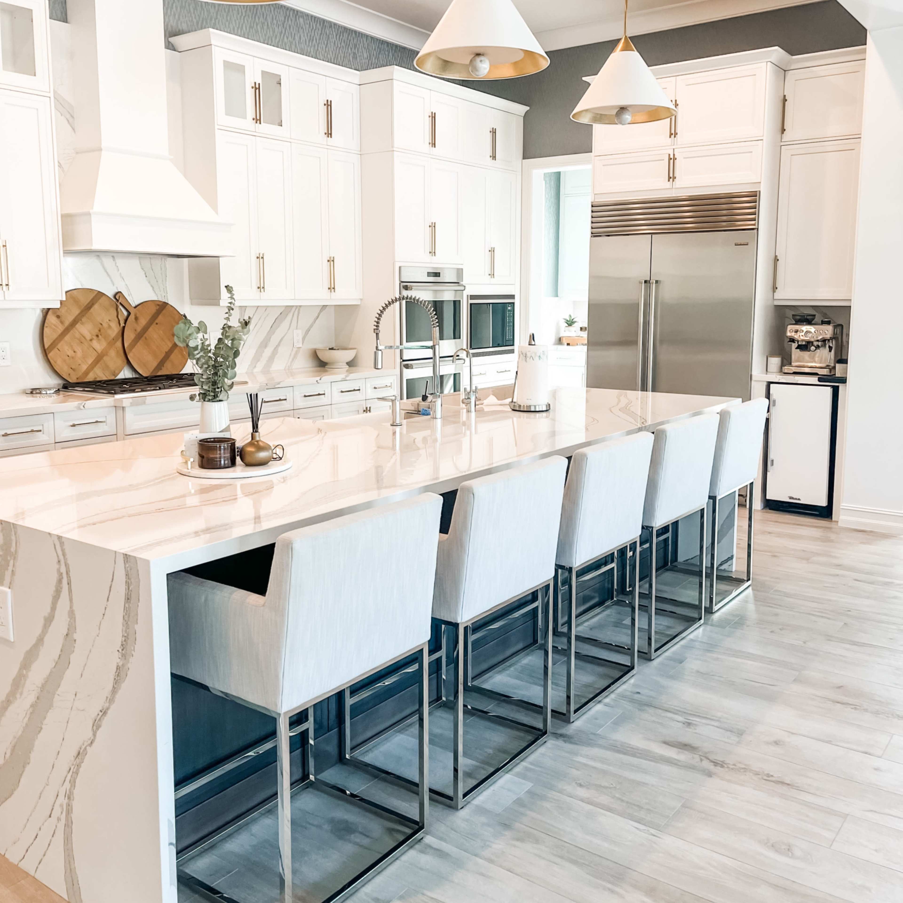 A modern kitchen features a large island with bar seating, white cabinetry, and pendant lighting.