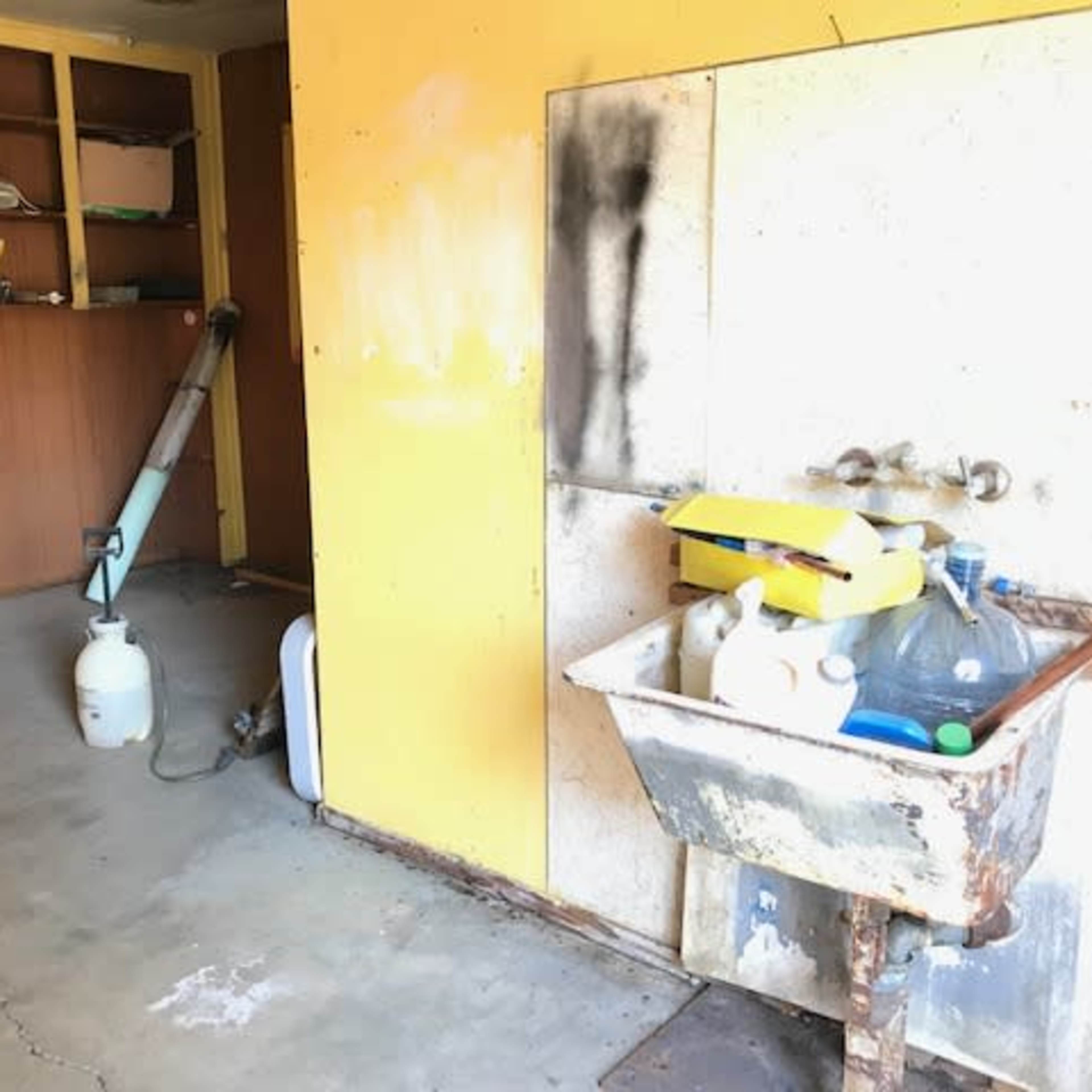 A partially empty room with a sink, visible cleaning supplies, a vacuum cleaner, and yellow walls.