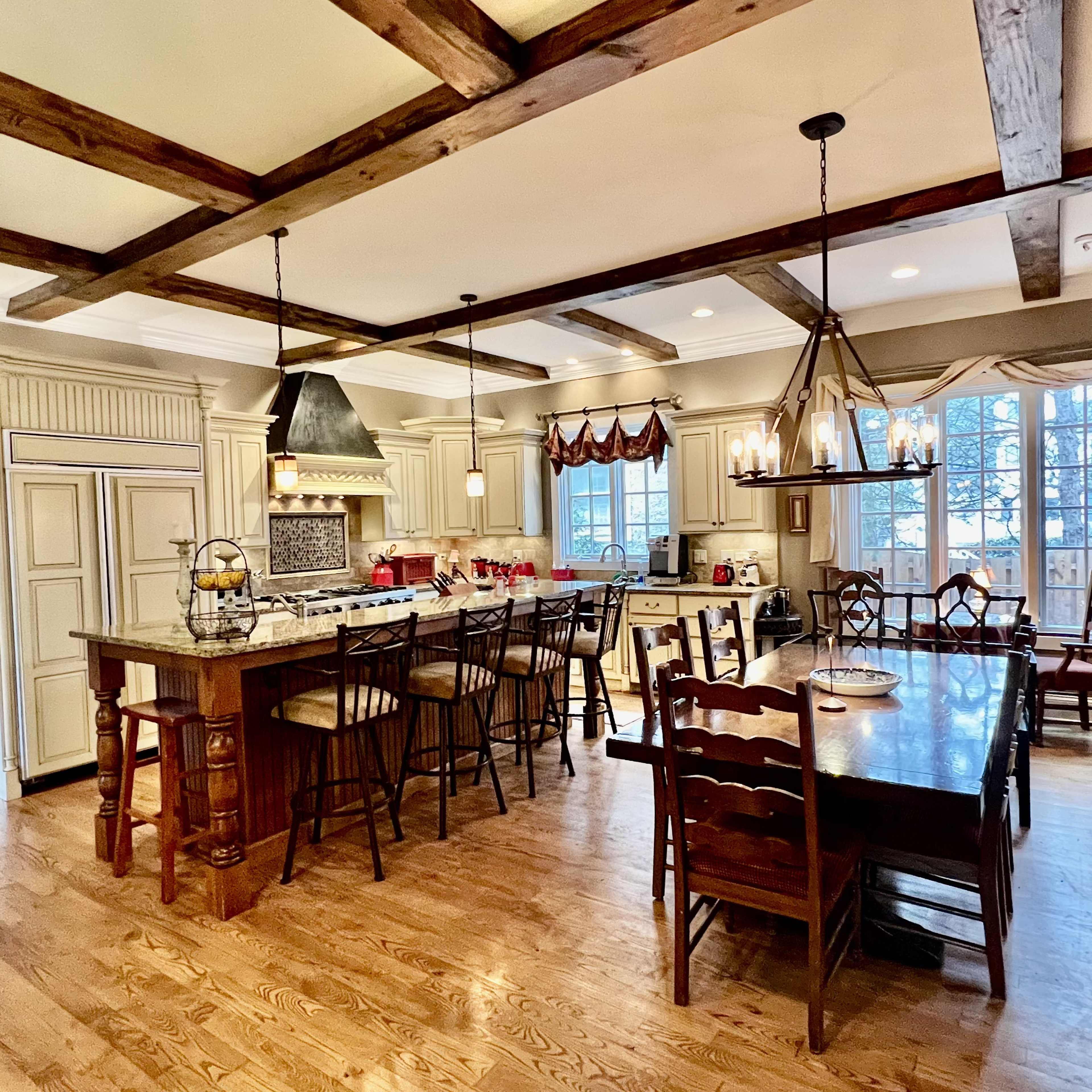 A spacious kitchen with a large island, wooden beams on the ceiling, and a dining area with a long wooden table and chairs.