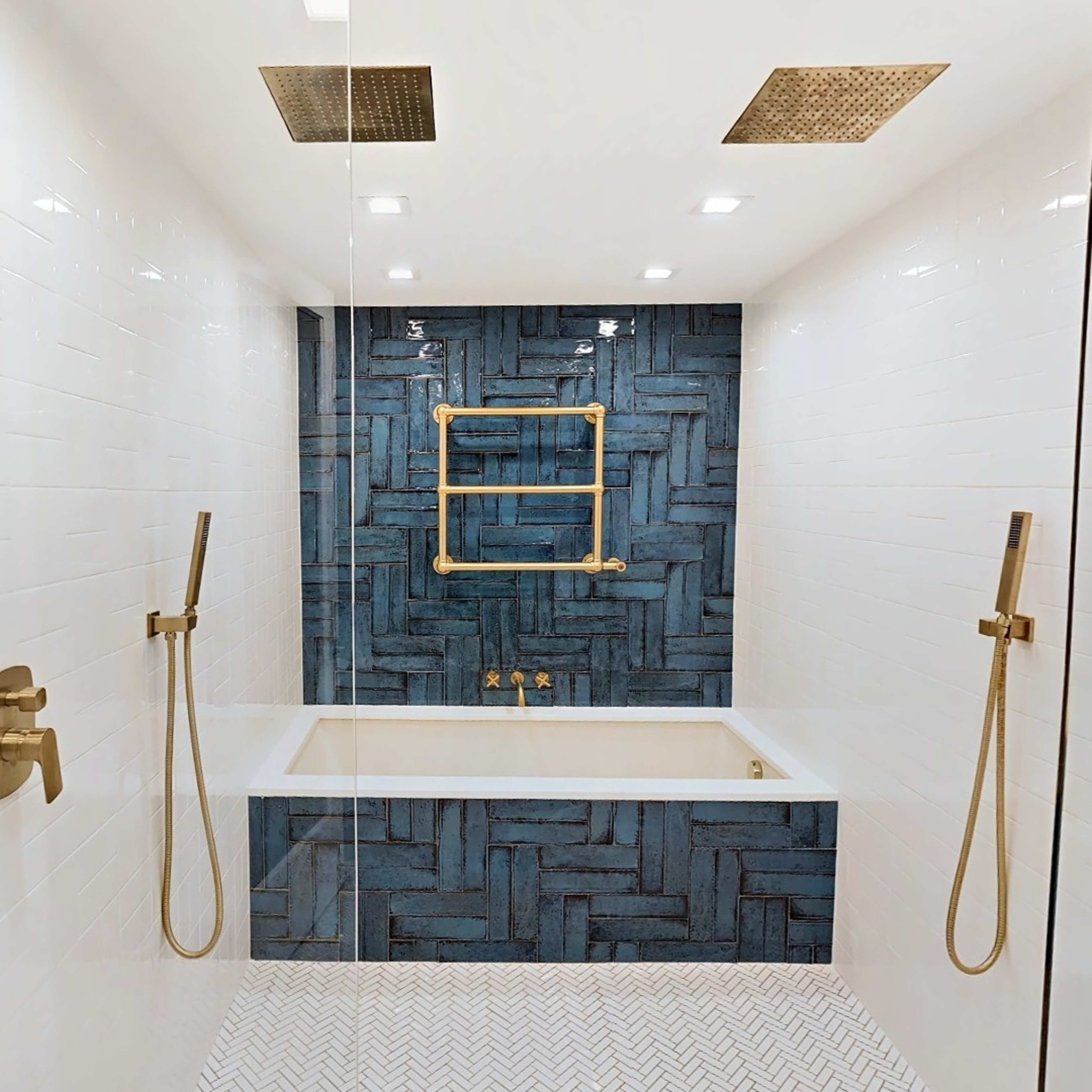 A modern bathroom featuring a blue patterned accent wall, a freestanding bathtub, and gold fixtures against white tiled walls.