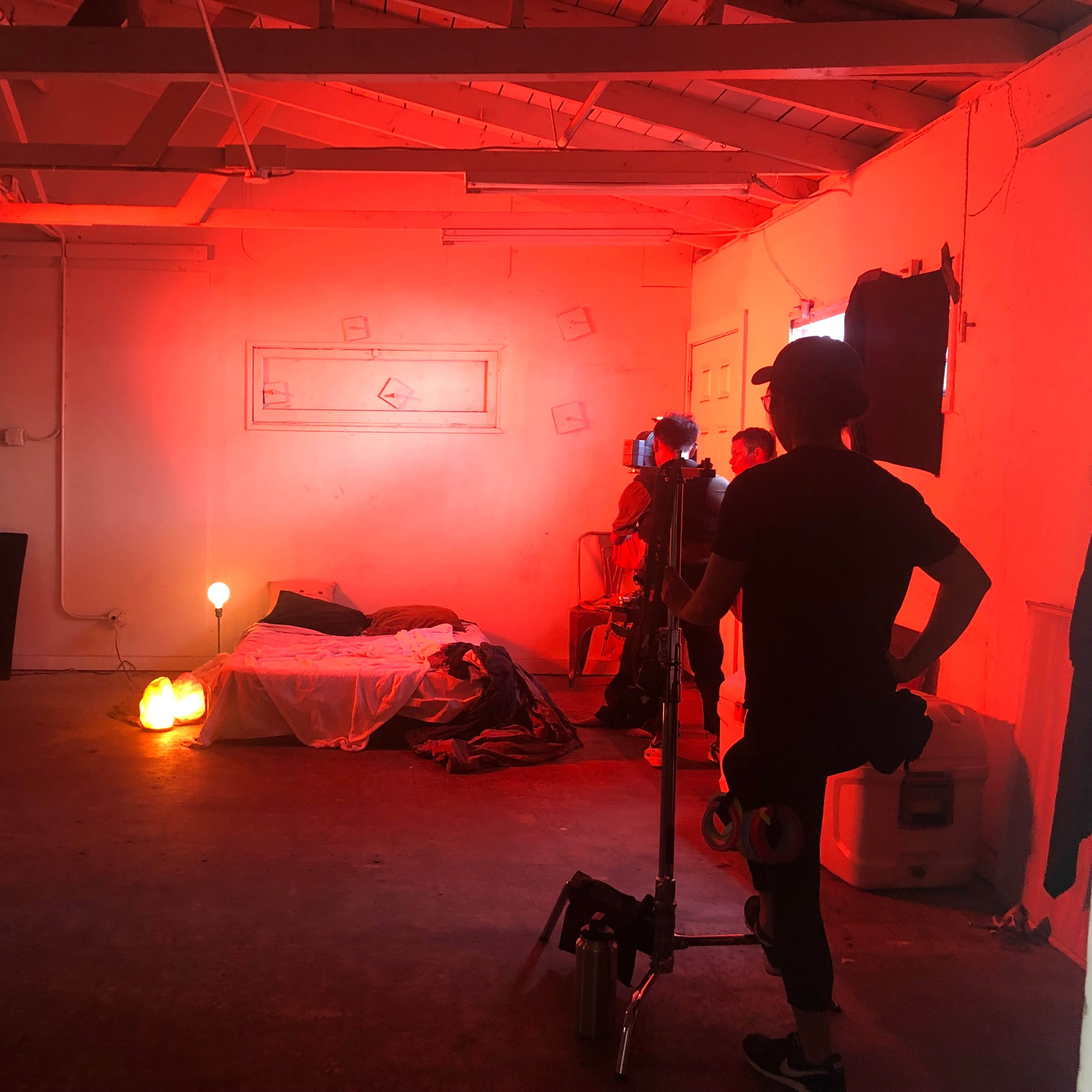 A dimly lit room featuring a bed, props, and various lighting equipment set up for a shoot.