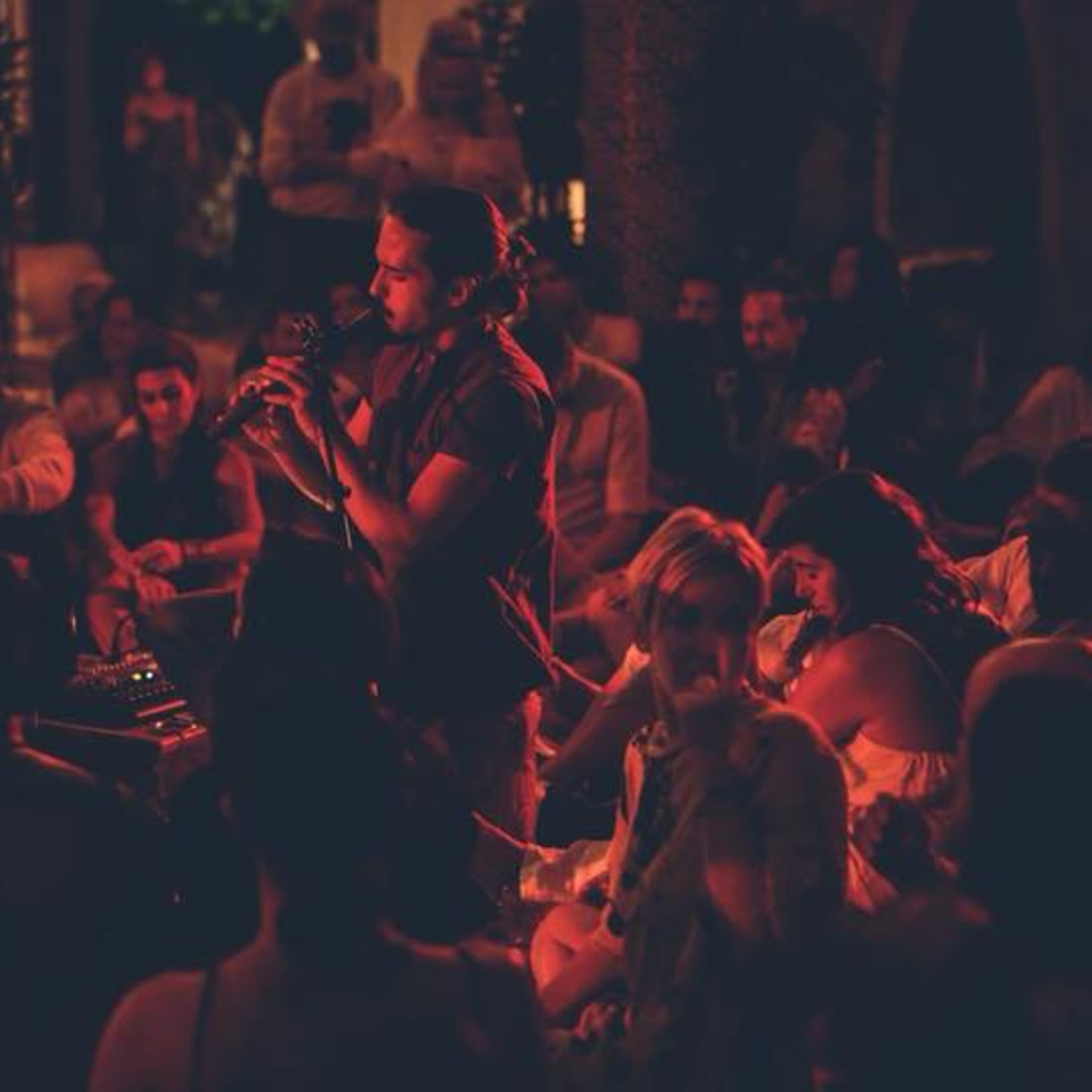 A singer performs onstage while an audience sits closely around, illuminated by soft lights in an outdoor setting.