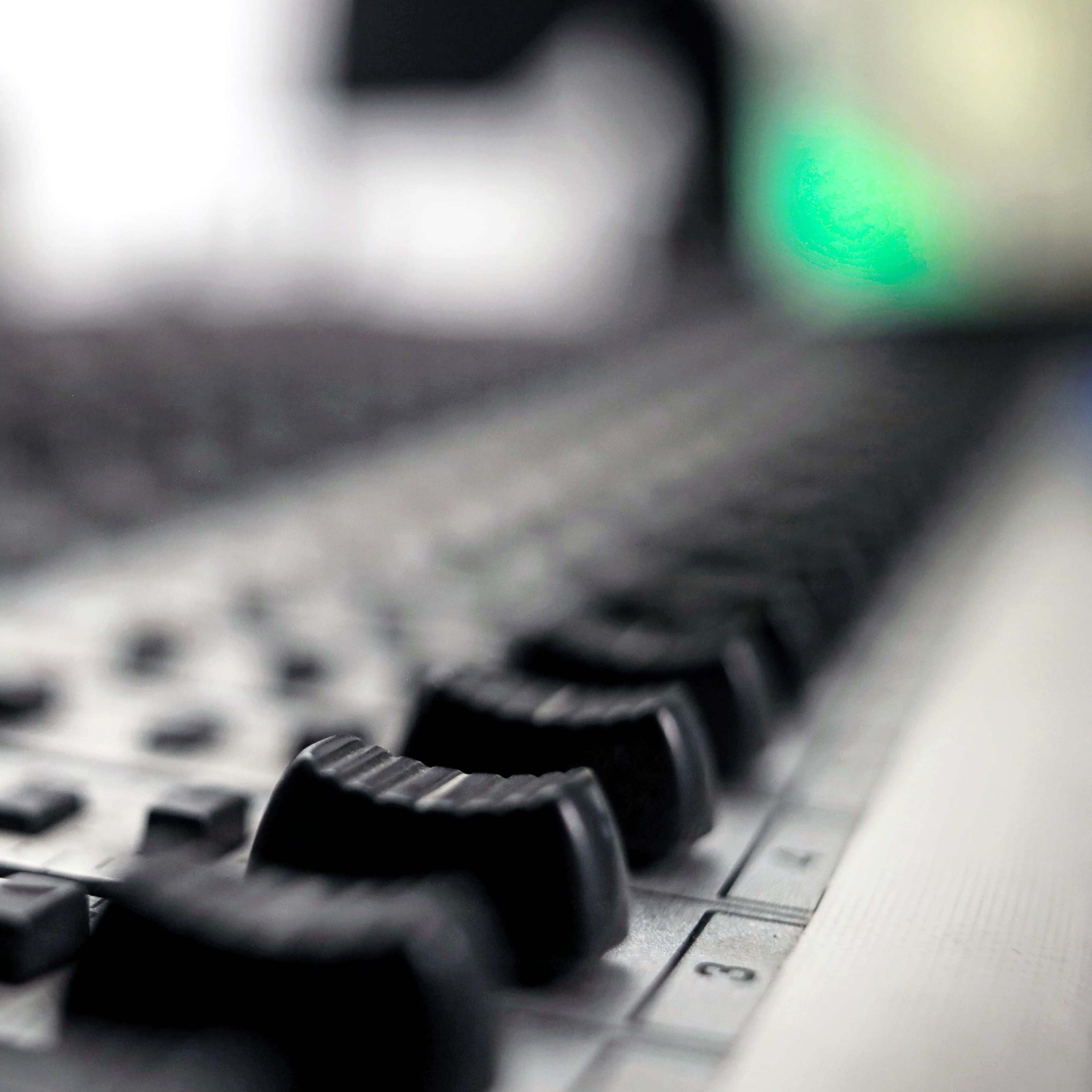 A close-up of a sound mixing console featuring various knobs and buttons arranged in rows.